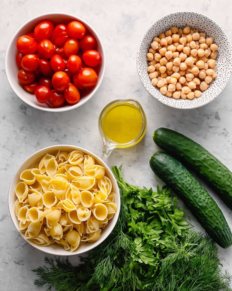 The image shows an arrangement of fresh ingredients on a white marbled surface. At the top left, there is a white bowl filled with small, bright red cherry tomatoes. To the top right, a patterned white bowl holds light beige chickpeas. Below the tomatoes, a larger white bowl contains dry, yellow shell pasta. In the center, there is a small glass pitcher with yellow dressing or sauce. To the right of the pitcher, two whole dark green cucumbers lie side by side. Below the cucumbers, fresh green herbs including dill and parsley are placed, creating a vibrant contrast with the other ingredients. photo taken with an iphone --ar 4:5 --v 7