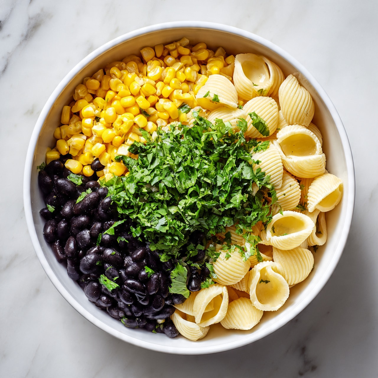A large white bowl with layers of food is on a white marbled surface. The bottom layer is light yellow shell pasta with a smooth texture. On top of that is a layer of bright yellow corn kernels, scattered evenly. Above the corn is a layer of black beans, dark and shiny, covering part of the corn. The top layer is fresh green cilantro leaves, chopped and spread over the beans and corn, adding a fresh look. The bowl is full and the colors of yellow, black, and green stand out clearly. Photo taken with an iphone --ar 4:5 --v 7