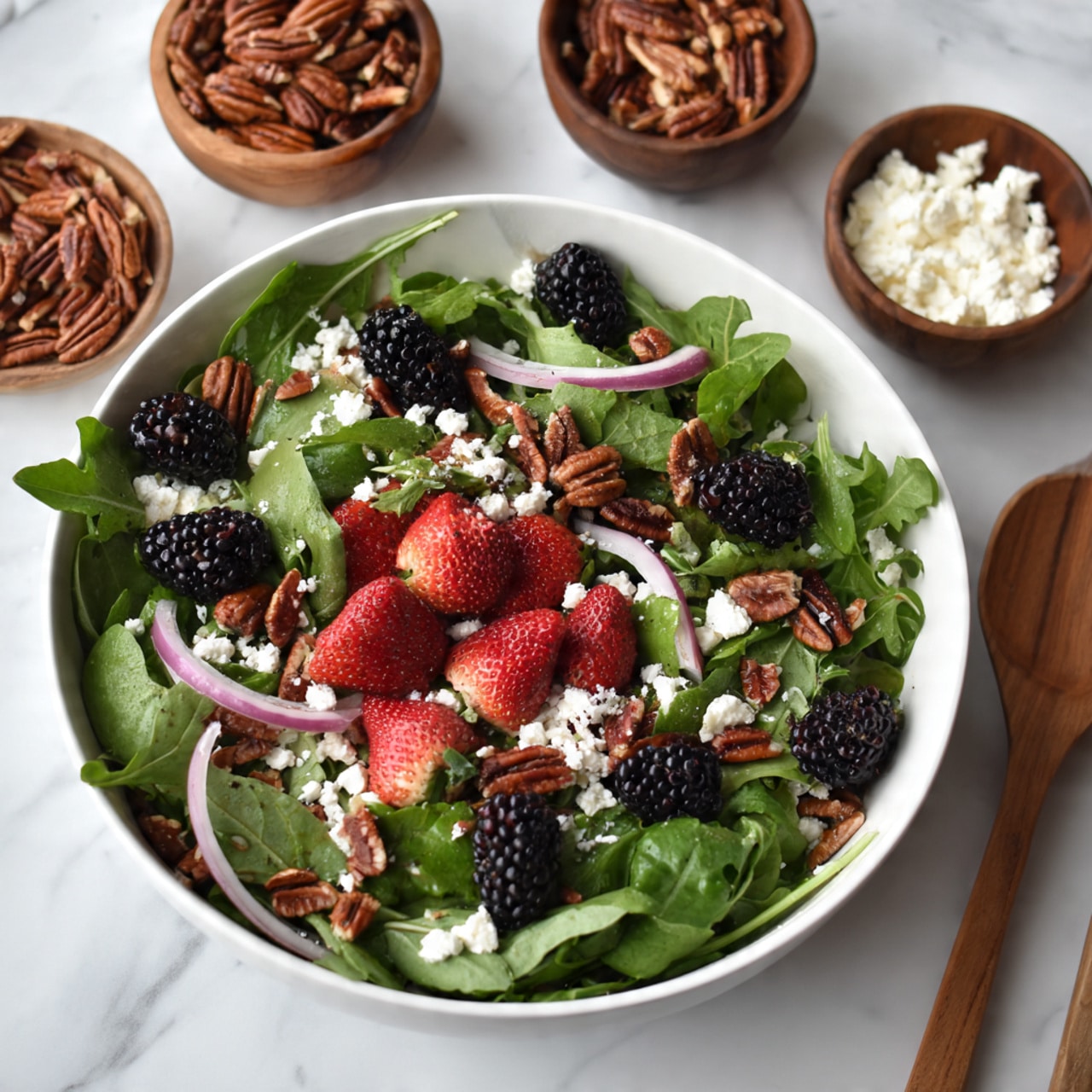 A fresh salad in a white bowl on a white marbled surface has several layers. The base layer is green arugula leaves, giving a leafy texture. On top, there are red strawberry pieces and black blackberries, adding bright color spots. Thin, light pink onion slices are scattered evenly, mixed with small white crumbles of cheese. Brown pecan nuts are spread across the salad adding a rich texture. Around the bowl, there are small wooden bowls with pecans and white cheese, along with a wooden salad fork visible in the bottom right corner. Photo taken with an iphone --ar 4:5 --v 7