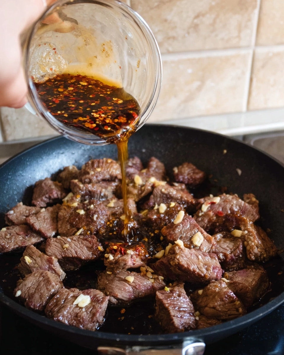 A close-up of a black pan on a white marbled surface with several pieces of browned, cooked beef with bits of garlic on top inside. Above the pan, a woman's hand is pouring a dark sauce with small chili flakes from a clear glass bowl onto the beef. The beef pieces are arranged in a scattered way, showing a mix of brown cooked parts and pinkish raw edges. The background shows a beige tiled wall. photo taken with an iphone --ar 4:5 --v 7