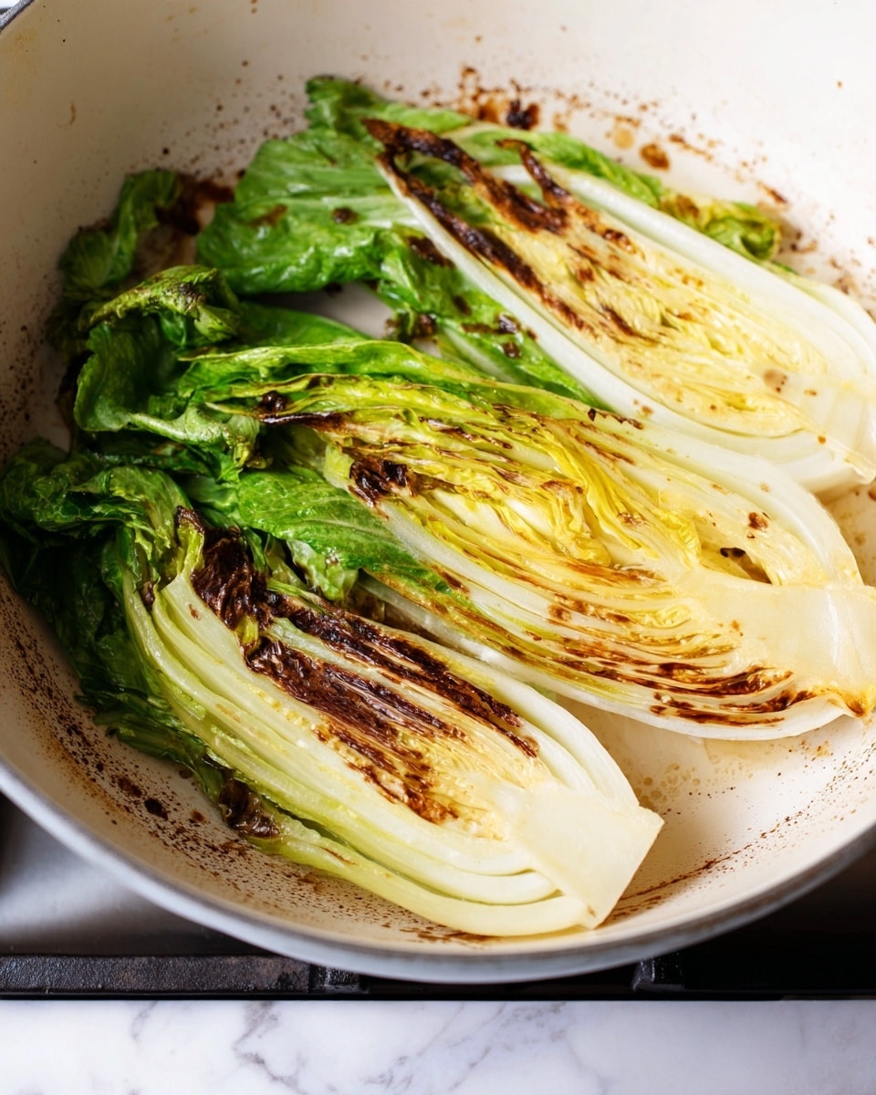 The image shows two halves of a leafy vegetable pan-seared in a white pot on a stove. The vegetable has multiple layers with the outer leaves light green and the inner leaves pale yellow to white. The edges of the lower half have brown, charred marks from cooking, creating a contrast against the softer, uncooked-looking inner leaves. The texture is slightly wilted in some areas due to heat, and the white pot has some brown stains from the cooking process. The background is a white marbled texture. Photo taken with an iphone --ar 4:5 --v 7