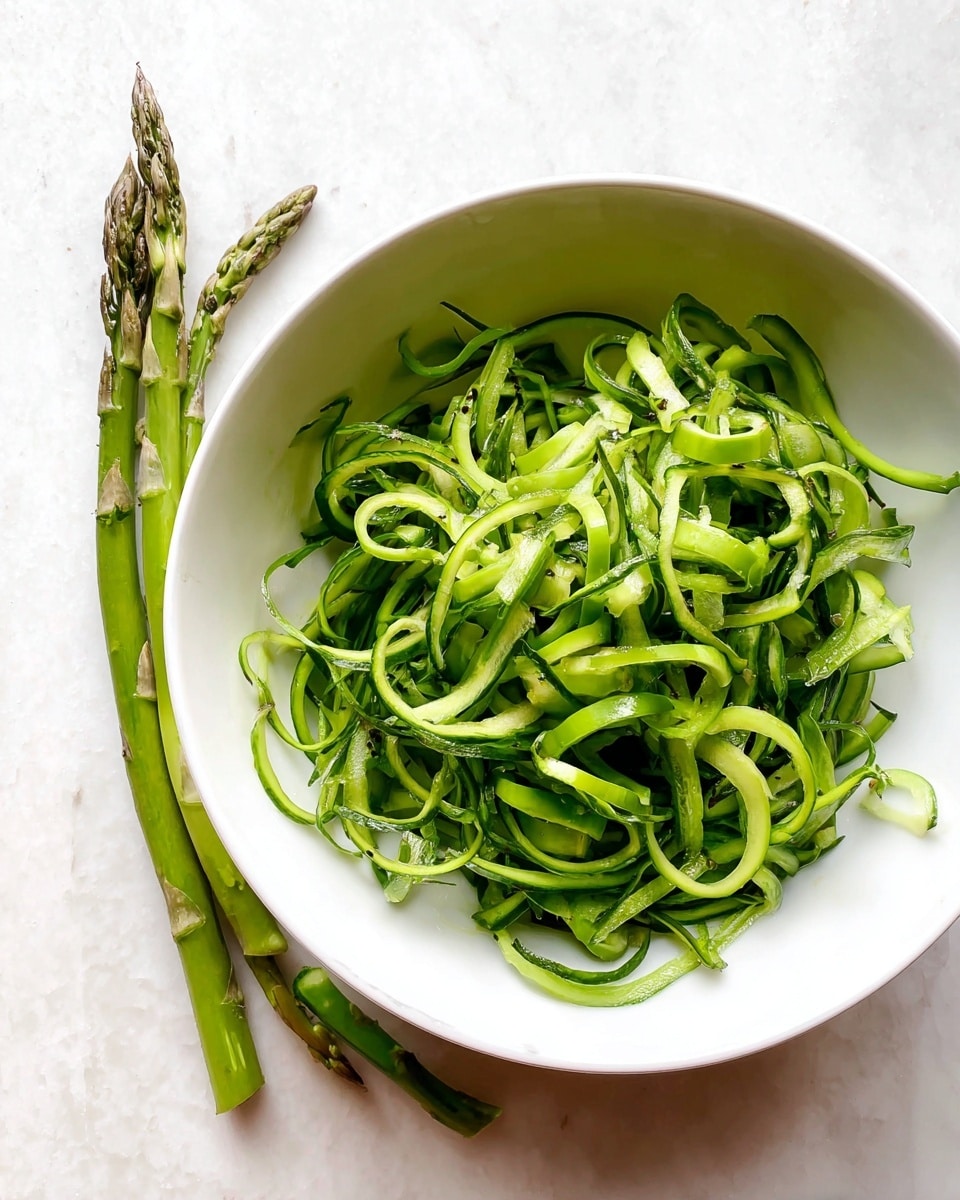 A white bowl filled with thin, curly green asparagus peelings and a few whole asparagus stalks, all showing bright green shades with a fresh, slightly shiny texture, placed on a surface with white marbled texture photo taken with an iphone --ar 4:5 --v 7