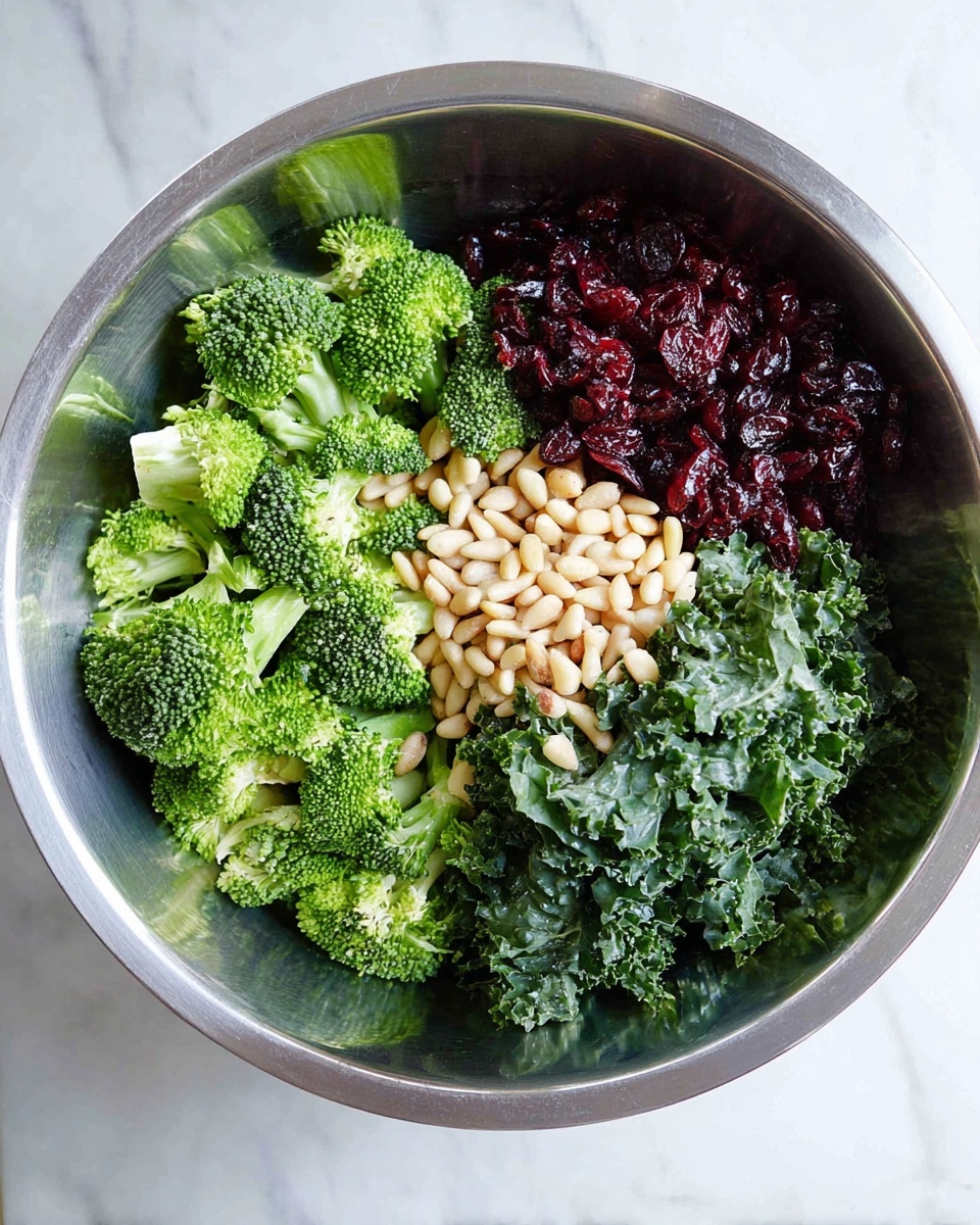 A large silver bowl sits on a white marbled surface, filled with a fresh salad arranged in four layers. One side of the bowl is packed with bright green broccoli florets with a firm texture. Next to the broccoli, there is a layer of dark red dried cranberries, looking slightly shiny and wrinkled. On the opposite side, there is a bed of curly, dark green kale leaves, rough and leafy in texture. On top of the kale, a neat pile of small, pale beige pine nuts adds a smooth and shiny contrast. photo taken with an iphone --ar 4:5 --v 7