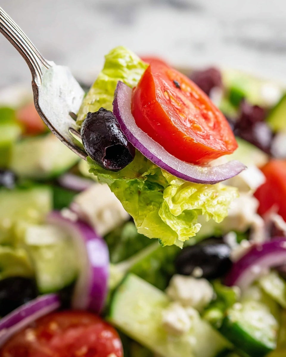 A fork holds a bite of fresh salad showing three main layers: bright green crisp lettuce leaves at the bottom, a round slice of red tomato in the middle, and a shiny dark purple olive along with a thin ring of light purple onion on top. The background is filled with more salad pieces including cucumber chunks, black olives, red onion slices, and white chunks of cheese, all placed on a white marbled surface. The colors are vivid with fresh textures of crunch and smoothness in the vegetables photo taken with an iphone --ar 4:5 --v 7