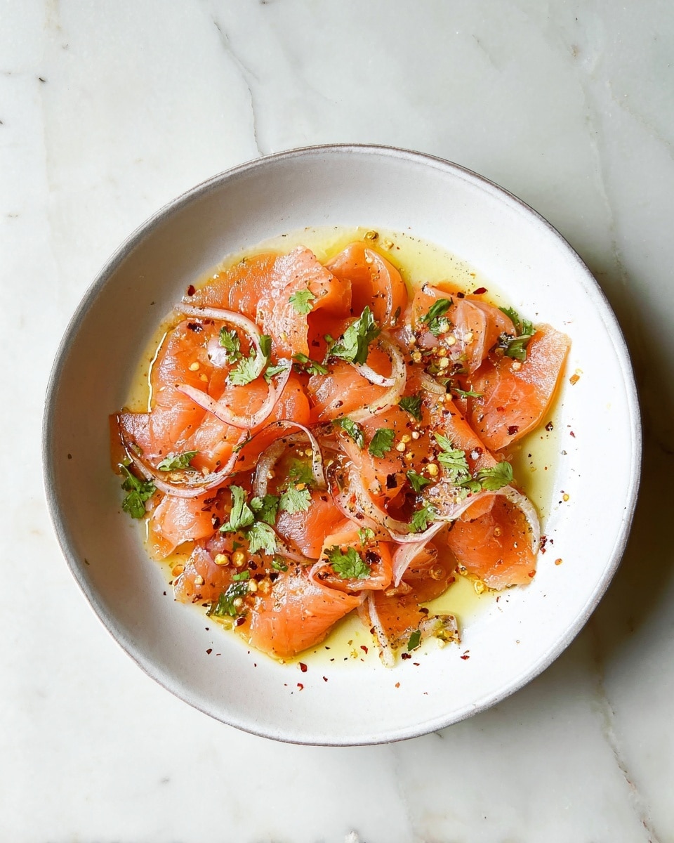 In a white bowl, there are several pieces of light orange raw salmon slices, each with a smooth and slightly shiny texture. The salmon is mixed with thin rings of pale pink shallots scattered on top and around. Green cilantro leaves are seen peeking through the layers of salmon. The dish is dressed with a light yellow-brown oily sauce, giving a glossy look. In the center, a small wedge of bright green lime with a pale, juicy inside adds a fresh contrast. Black pepper and red chili flakes are sprinkled lightly over the whole dish. The bowl sits on a white marbled surface, creating a clean, fresh background. photo taken with an iphone --ar 4:5 --v 7