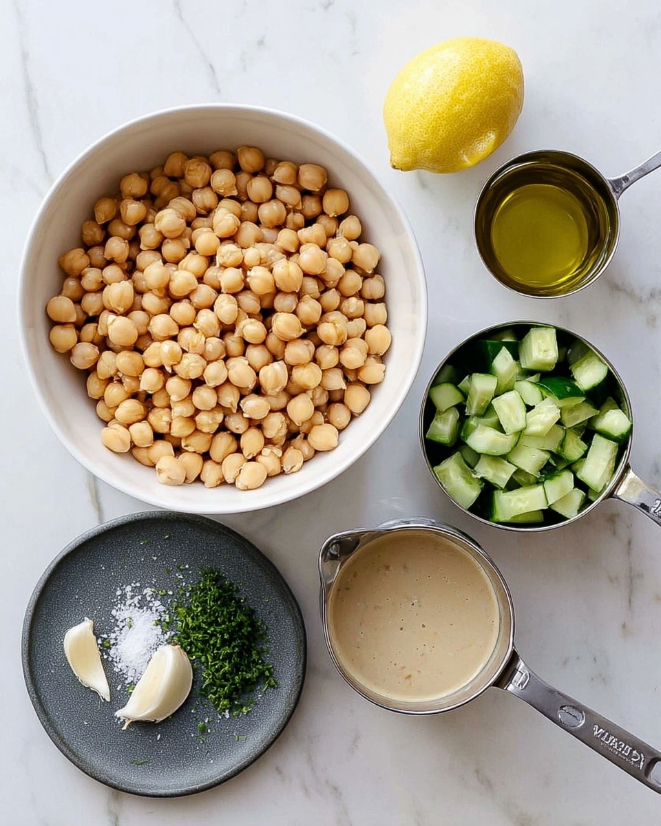 A white bowl filled with a large layer of light tan chickpeas in the center, surrounded by a metal measuring cup with chopped green cucumbers at the top right, a metal measuring cup with a beige creamy liquid at the bottom right, and a white container with olive oil at the top left. At the bottom left, there is a small dark gray round plate with a layer of white salt, finely chopped green herbs, and a peeled small white garlic clove. A half lemon with a pale yellow flesh is placed above the measuring cup with the creamy liquid, all set on a white marbled surface. Photo taken with an iphone --ar 4:5 --v 7