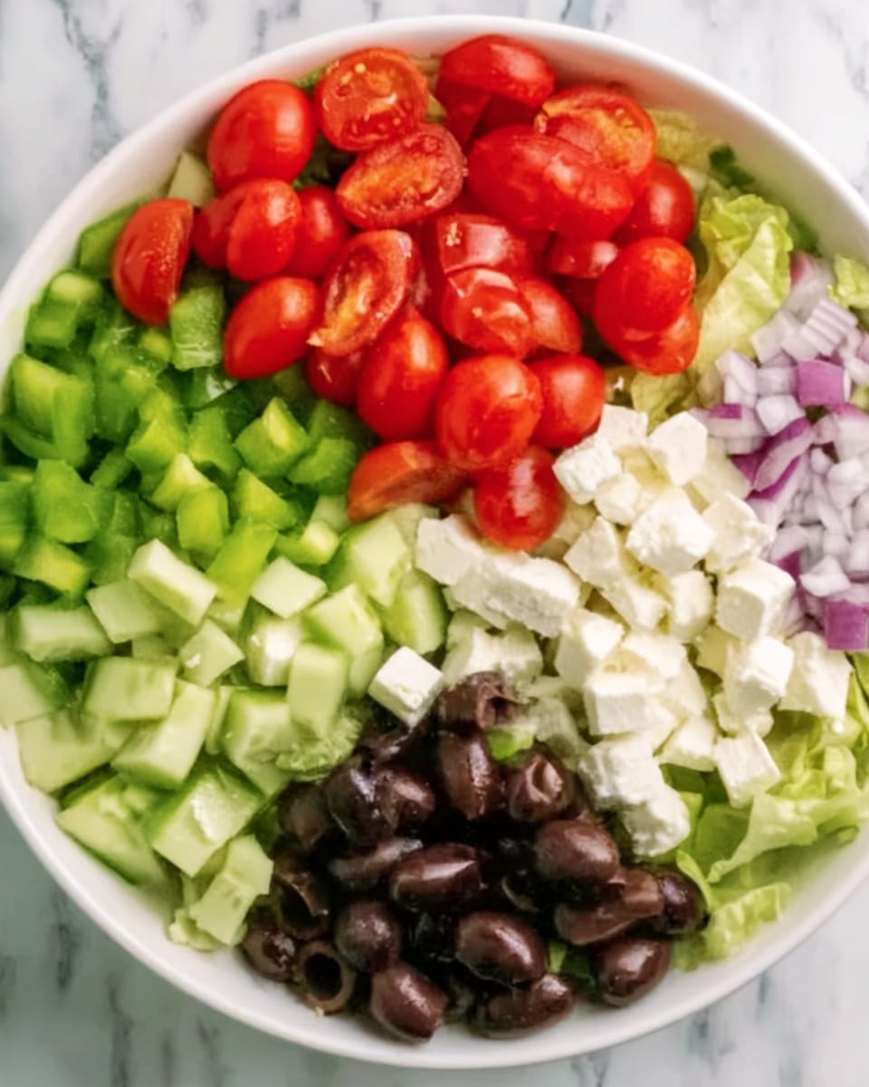 The image shows one white bowl filled with a colorful salad on a white marbled surface. The salad has five visible layers or sections: bright red grape tomatoes at the top, green chopped celery to the upper left, light green cucumber slices just below the celery, dark black olives below the tomatoes and some in the center, and white cubes of cheese to the right of the olives. There are also some pale purple onion rings on the far right edge above the cheese. The colors are fresh and vibrant, and the textures vary from smooth tomatoes to crunchy celery and soft cheese. Photo taken with an iphone --ar 4:5 --v 7