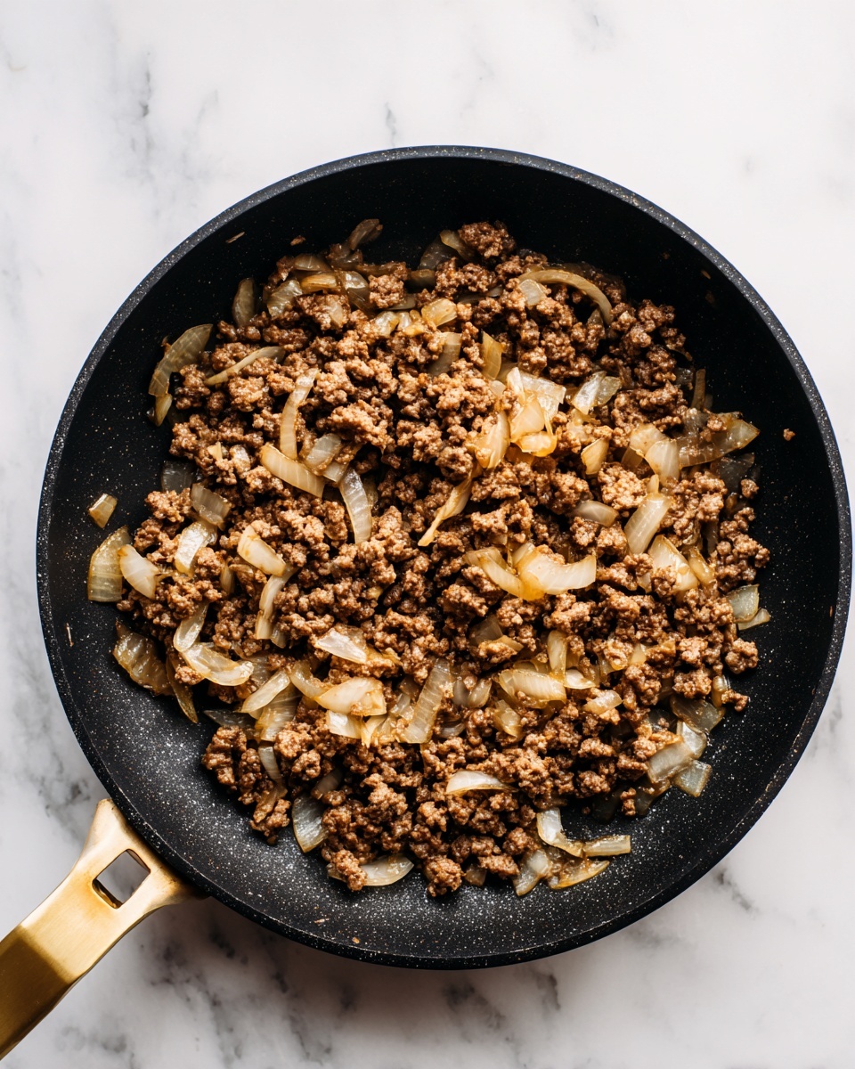 A black frying pan with a golden handle filled with two layers of cooked ingredients: the bottom layer is small, crumbly browned ground meat, and scattered throughout are small pieces of slightly translucent sautéed onions that have hints of light brown from cooking. The pan rests on a white marbled surface with some natural light highlighting the textures of the meat and onions, showing the soft and slightly crisp parts. photo taken with an iphone --ar 4:5 --v 7