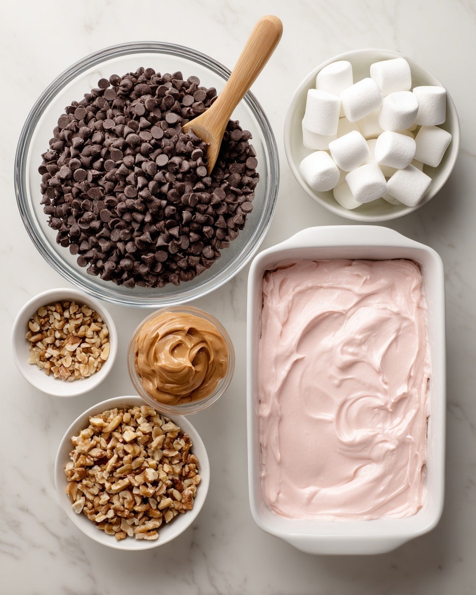A clear glass bowl is filled mostly with small dark brown chocolate chips, topped with a dollop of light brown peanut butter in the center; nearby is a smaller white bowl containing light brown chopped nuts. To the left, a larger clear measuring bowl holds small white marshmallows. Above these bowls is a small white dish filled with smooth pink frosting, next to a long wooden spoon with a round head. At the top center is a clean white rectangular baking dish. All items are placed on a white marbled surface. Photo taken with an iphone --ar 4:5 --v 7