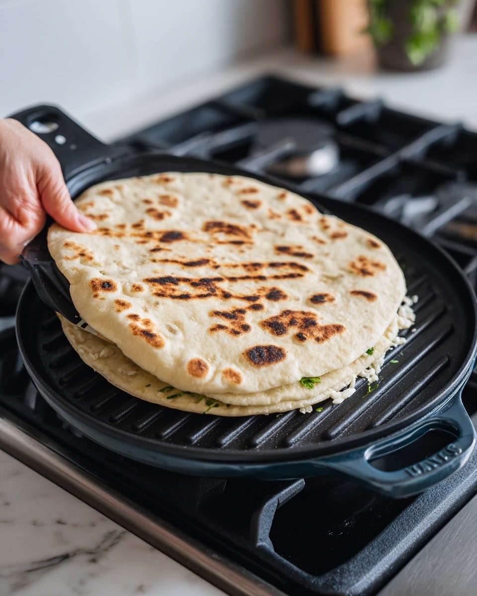 A round folded tortilla with clear, dark grill marks on the top layer sits in a black round grill pan with dark blue handles. The tortilla is light beige with some browned spots and has a few green leaves and white melted cheese peeking out from the edge. A black spatula, held by a woman's hand, is lifting the tortilla slightly from the pan. The background includes a black stove surface and a white marble texture counter is partially visible. photo taken with an iphone --ar 4:5 --v 7