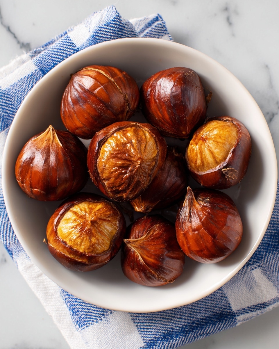 A white bowl holds eight shiny caramelized chestnuts with a rich golden brown color and slightly wrinkled texture, each chestnut appearing soft and glistening with a sticky glaze, arranged in a small pile in the center of the bowl, all set on a white marbled surface with part of a white cloth featuring blue grid lines visible in the background, photo taken with an iphone --ar 4:5 --v 7
