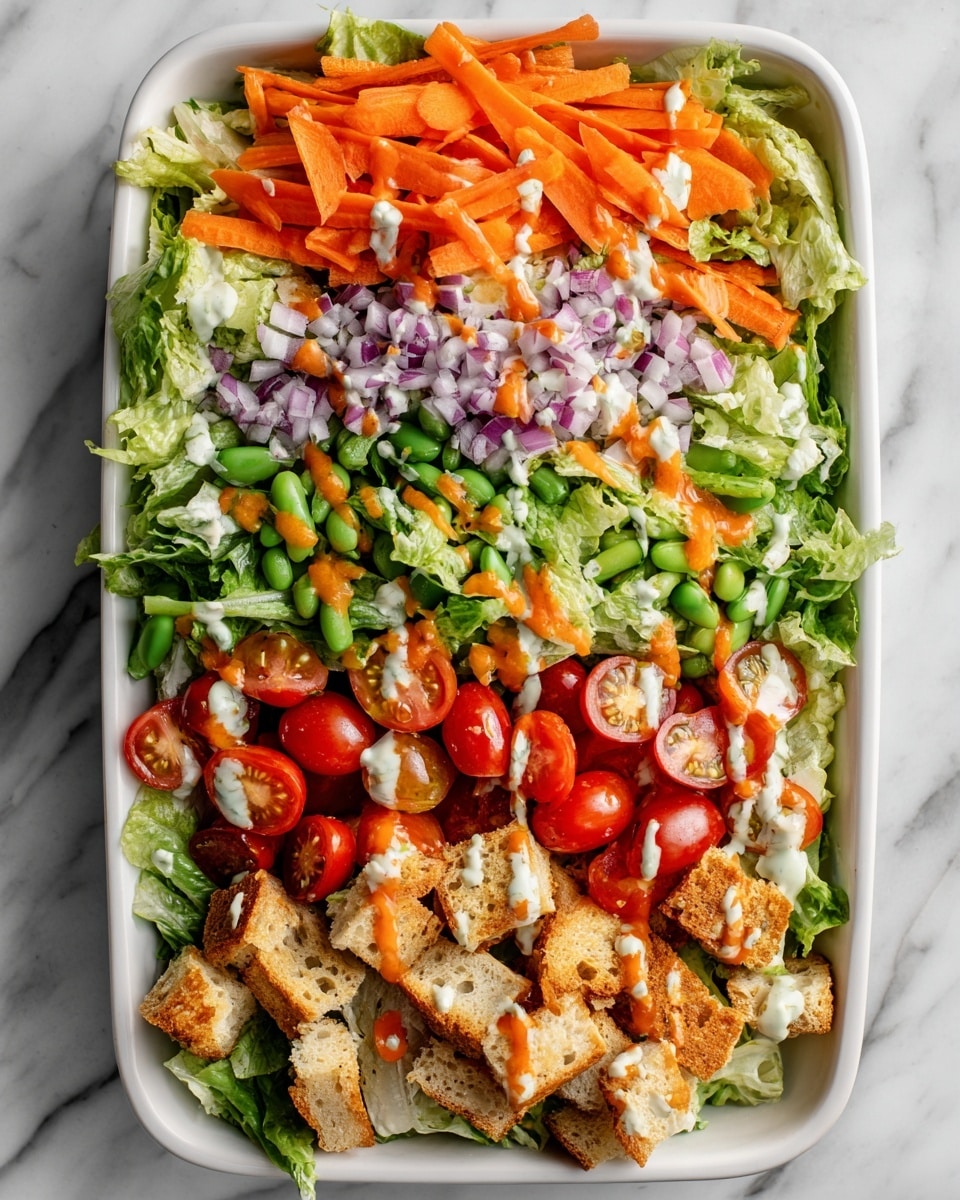 A white rectangular dish is filled with a mixed salad with several layers: bright green leafy lettuce pieces form the base layer, topped with orange carrot strips, halved red cherry tomatoes, light green snap peas, small bits of red onion, and scattered creamy white crumbled cheese. Golden brown, crispy textured pieces of cooked food, likely seasoned, are spread evenly on top. Two wooden spoons rest in the salad, one on the left side and one on the right. The dish is placed on a white marbled surface with a folded striped cloth nearby. Photo taken with an iphone --ar 4:5 --v 7