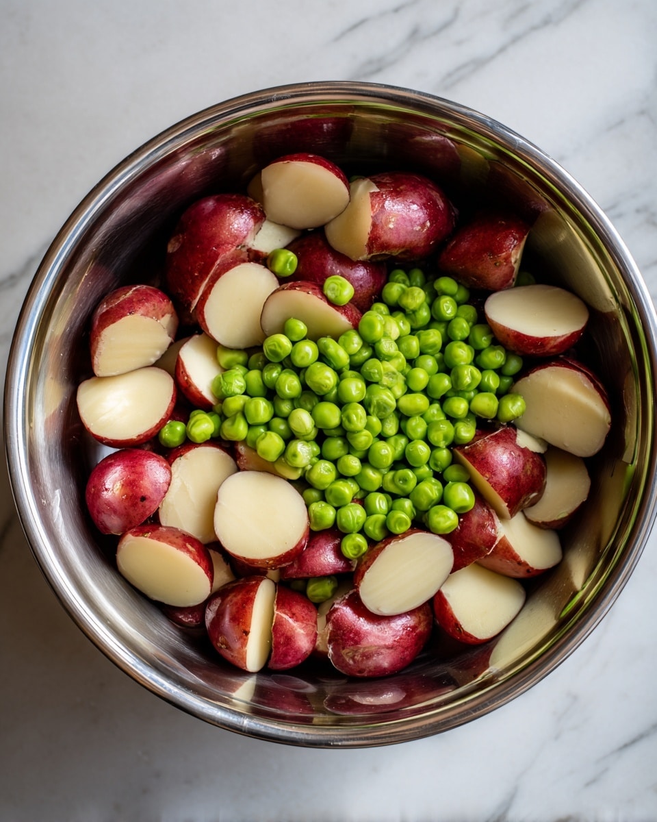 Inside a shiny metal bowl, there are two main layers of food. The bottom layer is bright, round green peas scattered evenly, showing a fresh texture. On top of the peas are many pieces of red-skinned potatoes, each piece cut into halves or quarters, showing their smooth off-white inside. The potato pieces are spread out, mixing with the peas, creating a contrast of red and green colors. The bowl sits on a white marbled surface, with soft natural light reflecting off the metal. photo taken with an iphone --ar 4:5 --v 7