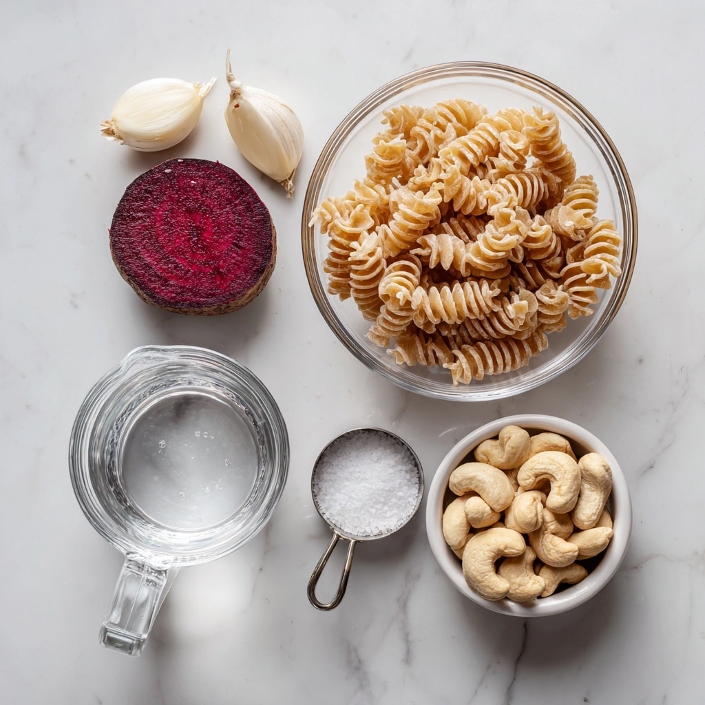 The image shows five separate items arranged on a white marbled surface. On the right side, there is a clear glass bowl filled with dry pasta with a light brown color. Near it, there is a small clear glass bowl holding a round slice of dark red beet with a textured surface. Above the beet bowl, two peeled garlic cloves are placed next to a small metal measuring spoon filled with coarse white salt. On the lower right side, a white measuring cup is filled with raw cashews that have a pale beige color and smooth texture. Below and to the left of the pasta, there is a white measuring cup filled with clear water. The image is bright and clean, displaying each ingredient distinctly. photo taken with an iphone --ar 4:5 --v 7