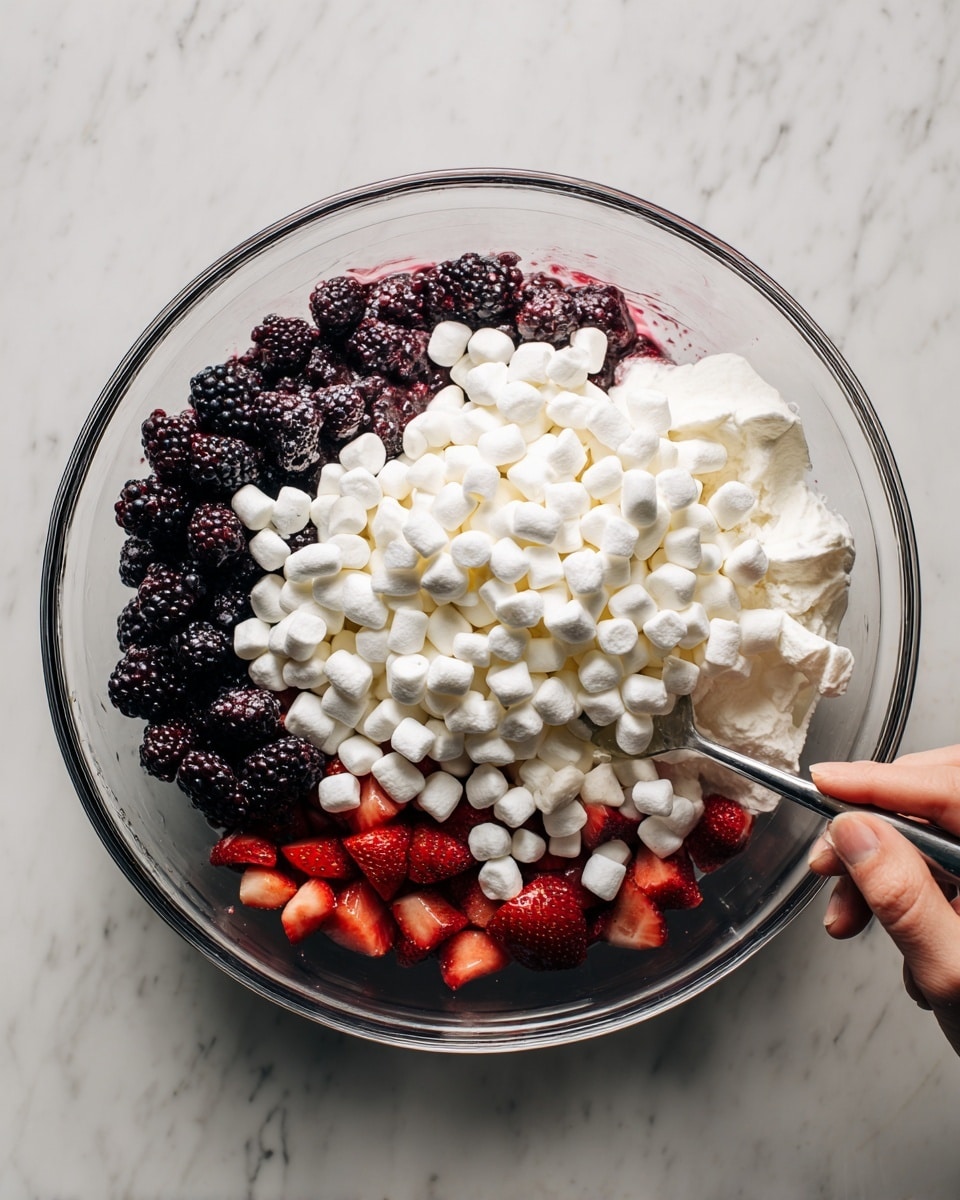 A clear glass bowl filled with a mix of three main layers: at the bottom, fresh blackberries and strawberries can be seen in dark purple and red colors; above them, there is a creamy white layer that is thick and smooth, partially covering the berries; on top, there is a large layer of small, white marshmallows that almost fill the bowl, showing their soft and fluffy texture. A woman's hand is visible on the right side, holding a spoon and mixing the contents. The bowl sits on a white marbled surface. photo taken with an iphone --ar 4:5 --v 7