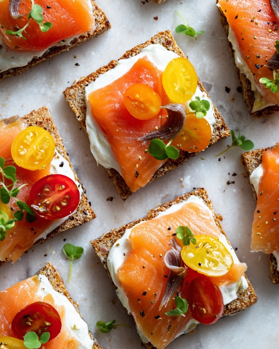 There are thirteen small square crackers on a white marble board. Each cracker has a base layer of white cream cheese spread evenly, topped with one or two slices of bright orange smoked salmon. On top of the salmon, there are thin slices of red and yellow cherry tomatoes and small green herb leaves scattered around. Some crackers have a thin slice of pickled red onion. The textures include the crispy cracker, smooth cream cheese, soft salmon, and fresh vegetables and herbs. Around the board, there is a white bowl with creamy dip speckled with red seasoning and a white plate with thin slices of salmon and lemon wedges. Photo taken with an iphone --ar 4:5 --v 7