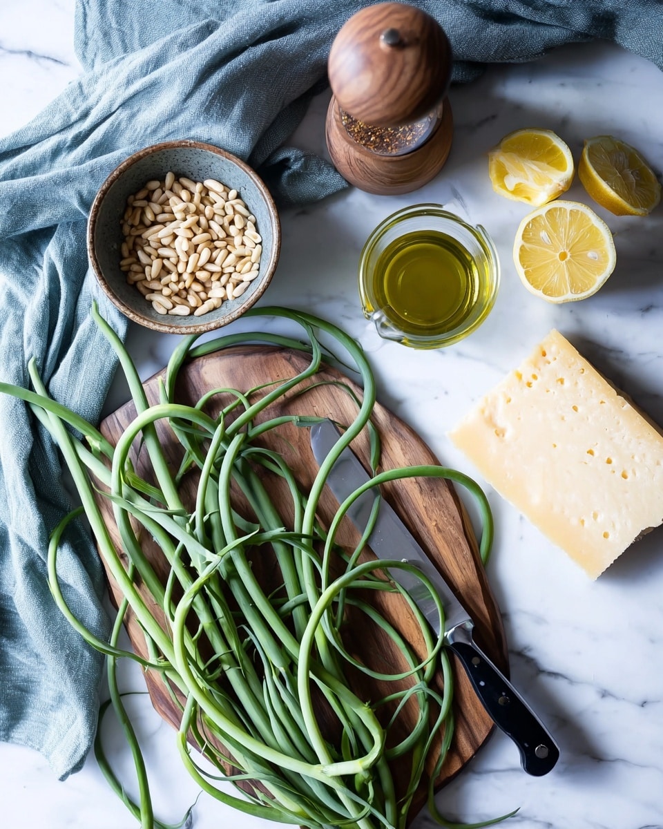 The image shows fresh ingredients arranged on a white marbled surface. There is a wooden cutting board holding several long, green garlic scapes curled in loose loops and a small black-handled knife with a silver blade. To the upper left of the cutting board are a bowl with pine nuts, a tall wooden container with a lid holding a spice mix, and a clear measuring cup filled with olive oil. Near the center top, two lemon halves and a large wedge of hard cheese sit directly on the surface. A soft blue-gray cloth partially covers the upper left corner. The photo is taken with an iphone --ar 4:5 --v 7