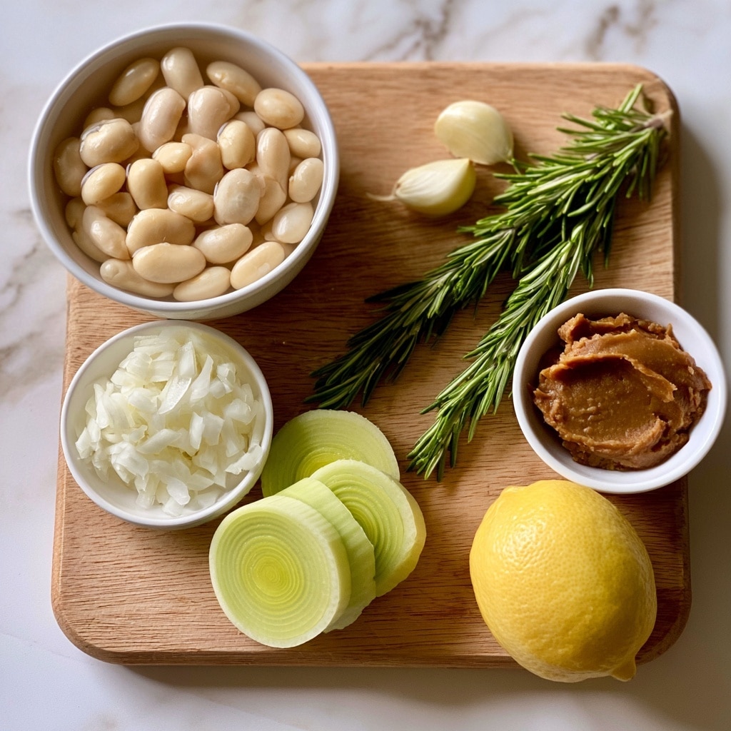 The image shows a wooden board placed on a white marbled surface, holding several ingredients for a recipe. On the left side, a white bowl filled with pale cream cannellini beans soaked in water is visible. Next to it, there is a small white bowl with finely chopped white onion. Below this, there are several round slices of light green leek stacked loosely. To the right, two sprigs of fresh green rosemary lie diagonally across the board, with two cloves of peeled garlic above them. Further right, a small white bowl contains a smooth, thick layer of brown miso paste. A whole bright yellow lemon sits at the bottom right corner of the board. The scene is lit softly, highlighting the fresh textures and natural colors of the ingredients, photo taken with an iphone --ar 4:5 --v 7