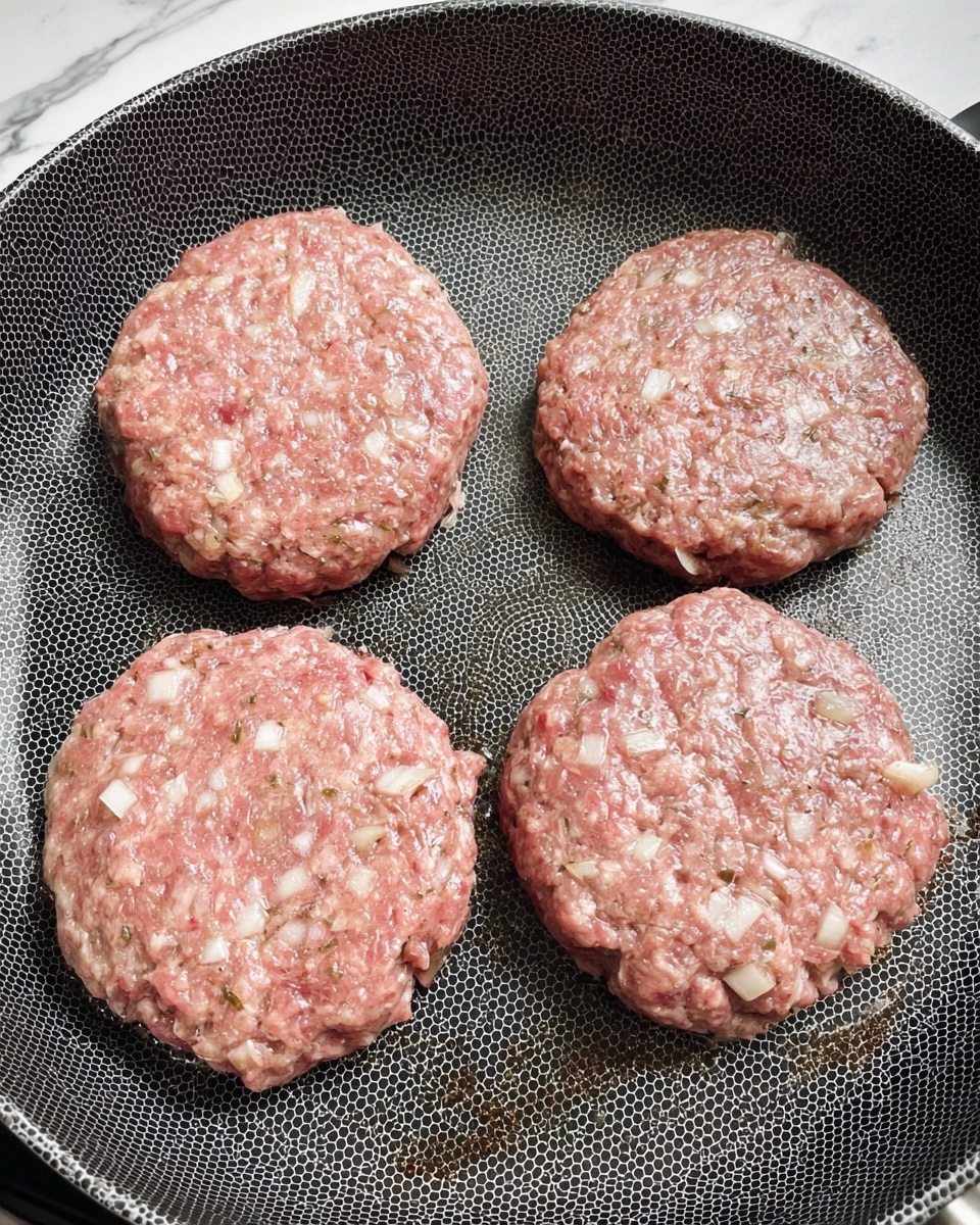 Four raw hamburger patties with visible white onion pieces mixed in are placed closely together on a non-stick frying pan with a honeycomb pattern. The patties show a mix of light pink and beige colors with a moist texture. The pan sits on a white marbled surface, with no other items visible. Photo taken with an iphone --ar 4:5 --v 7