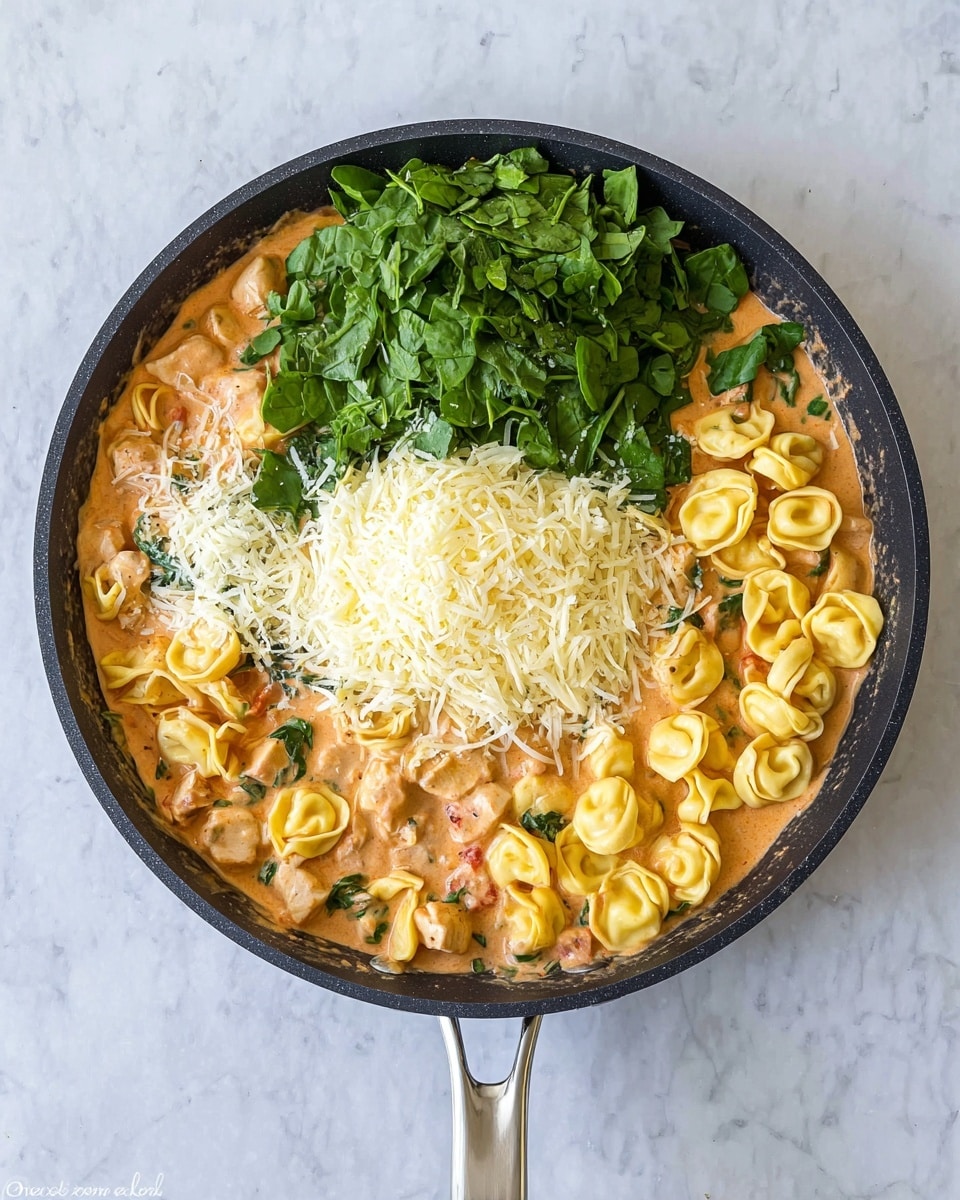 A black frying pan filled with a creamy light orange sauce mixed with yellow tortellini pasta and small pieces of chicken is placed on a white marbled surface. On top of the pasta in the center of the pan, there are three layers: a large pile of shredded white cheese on the left, fresh green spinach leaves in the middle, and a smaller pile of grated white cheese on the right. The pan handle is metallic and visible at the bottom of the image. photo taken with an iphone --ar 4:5 --v 7