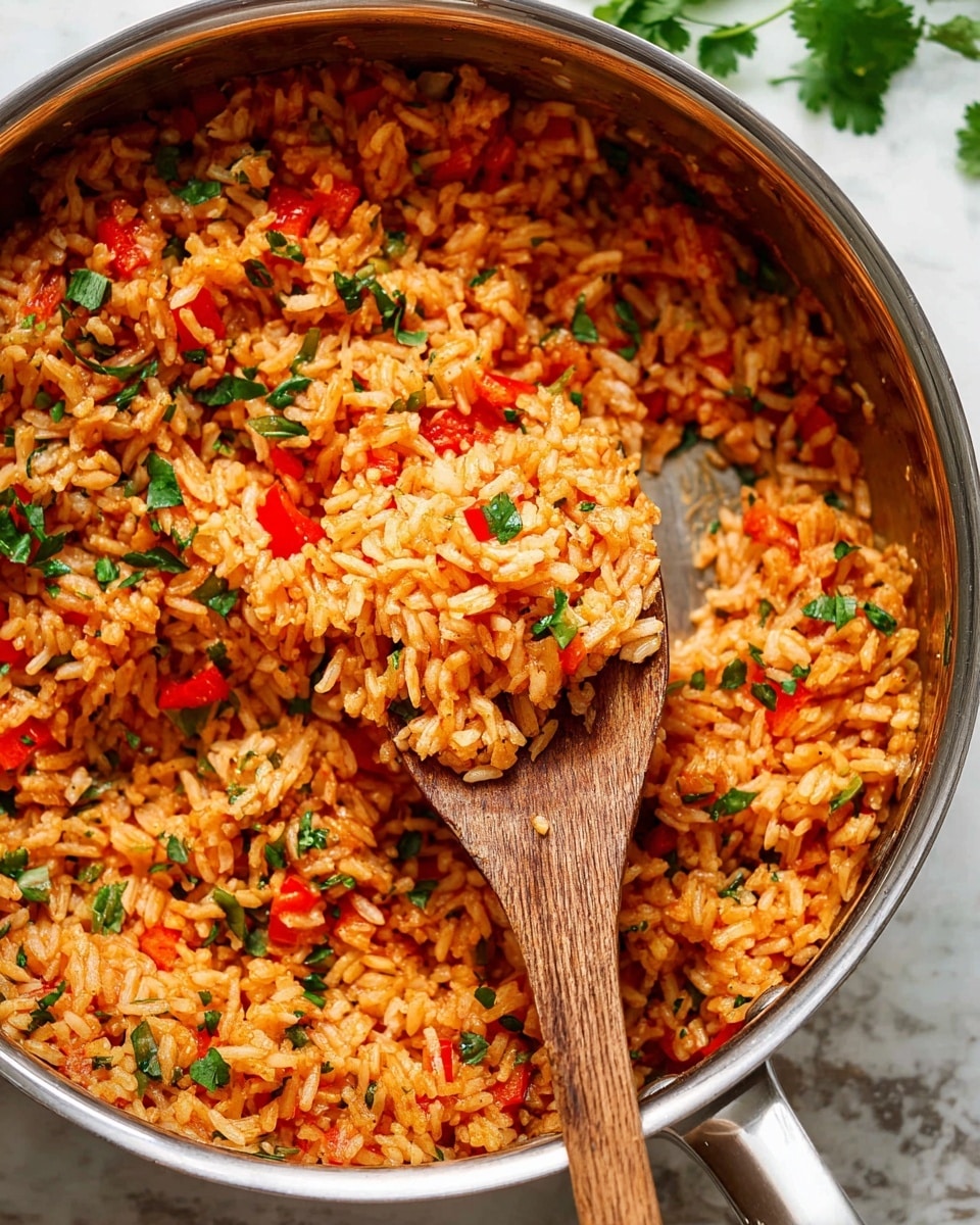 The image shows a close-up of a stainless steel pan filled with cooked Mexican rice. The rice is mostly orange-red with small pieces of red bell pepper, onion, and green herbs mixed evenly throughout. A wooden spoon is scooping a portion of the rice, showing the fluffy texture and colorful vegetable bits. The rice looks moist and well-cooked, with a slight shine and some chopped green herbs sprinkled on top for garnish. The background features a white marbled surface with some scattered cilantro leaves visible. photo taken with an iphone --ar 4:5 --v 7
