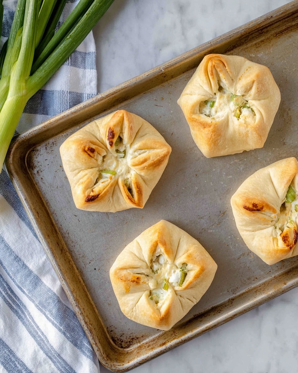 Four golden brown baked parcels sit on a metal baking tray. Each parcel is made from light beige dough, folded and pinched at the top into a flower-like shape with four visible folds. The dough has a slightly shiny and soft texture with some darker baked spots. Inside the parcels, a creamy white filling with small green pieces is visible through small openings near the folds. The tray is on a white marbled surface, with fresh green scallions partially visible at the top left corner next to a white and blue striped cloth. Photo taken with an iphone --ar 4:5 --v 7