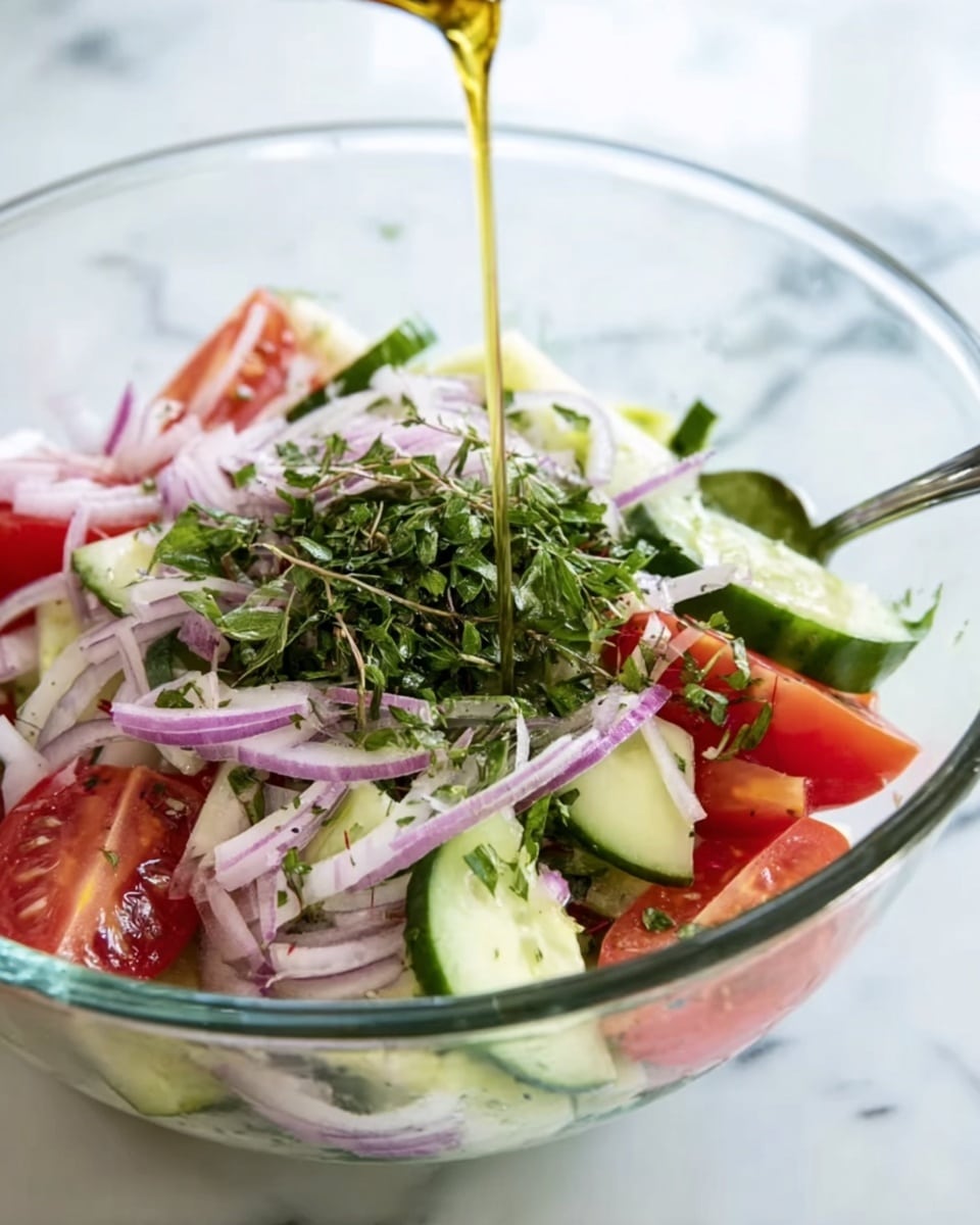 A clear glass bowl contains a fresh salad with visible layers of chopped red onions, sliced cucumbers, and quartered red tomatoes. Green herbs, likely cilantro or parsley, are sprinkled on top, adding texture and color. A golden liquid, probably dressing, is being poured over the salad from above. In the bowl, a metal spoon rests on the right side. The bowl is placed on a white marbled surface. Photo taken with an iphone --ar 4:5 --v 7