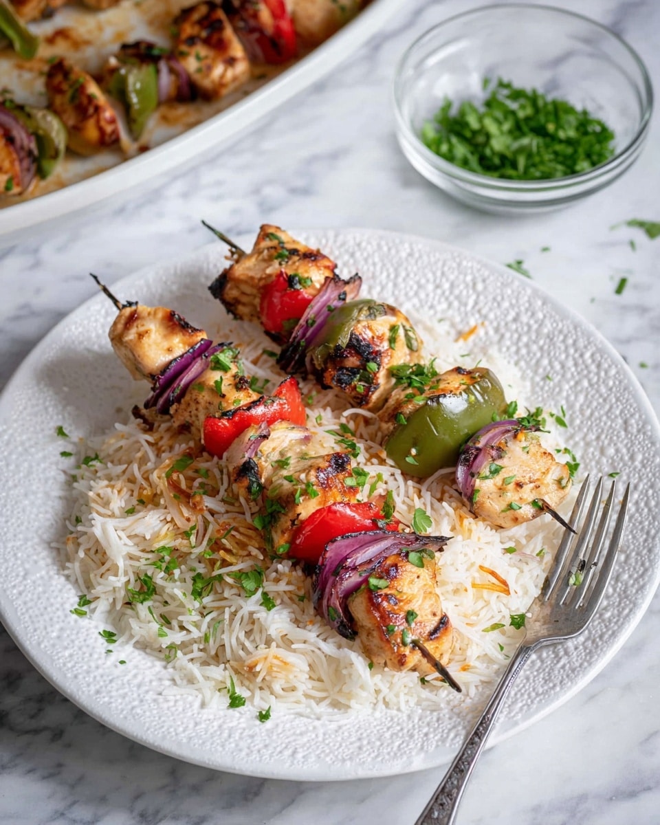 Two metal skewers of grilled pieces of light brown chicken, green bell pepper, red bell pepper, and purple onion sit on a bed of white rice mixed with golden toasted vermicelli noodles on a white textured plate. The rice is scattered with small bits of green chopped herbs. A silver fork lies on the plate's edge, and in the background, a clear glass bowl with chopped green herbs rests on a white marbled surface next to a larger white dish with more of the chicken skewers and rice. photo taken with an iphone --ar 4:5 --v 7