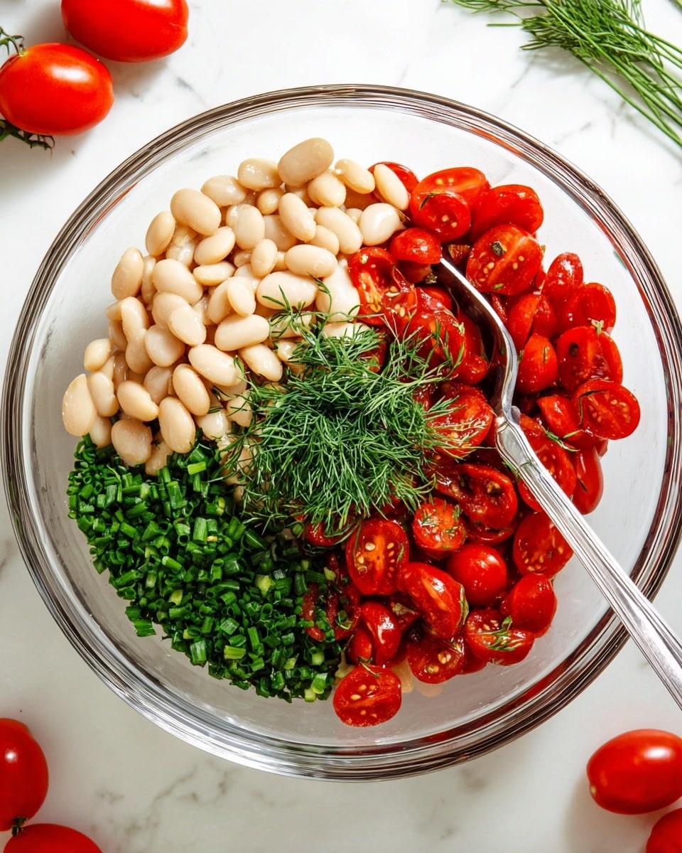 A clear glass bowl placed on a white marbled surface holds a colorful mixture divided into four layers: a large pile of smooth, creamy white beans fills the bottom left part; bright red, round cherry tomatoes, some cut in halves, take up the bottom right section; finely chopped dark green chives form a dense patch above the beans; and a small bunch of feathery, dark green dill sits above the tomatoes. A shiny silver spoon is resting inside the bowl near the herbs. Around the bowl, a few whole red tomatoes and green herbs can be seen. Photo taken with an iphone --ar 4:5 --v 7