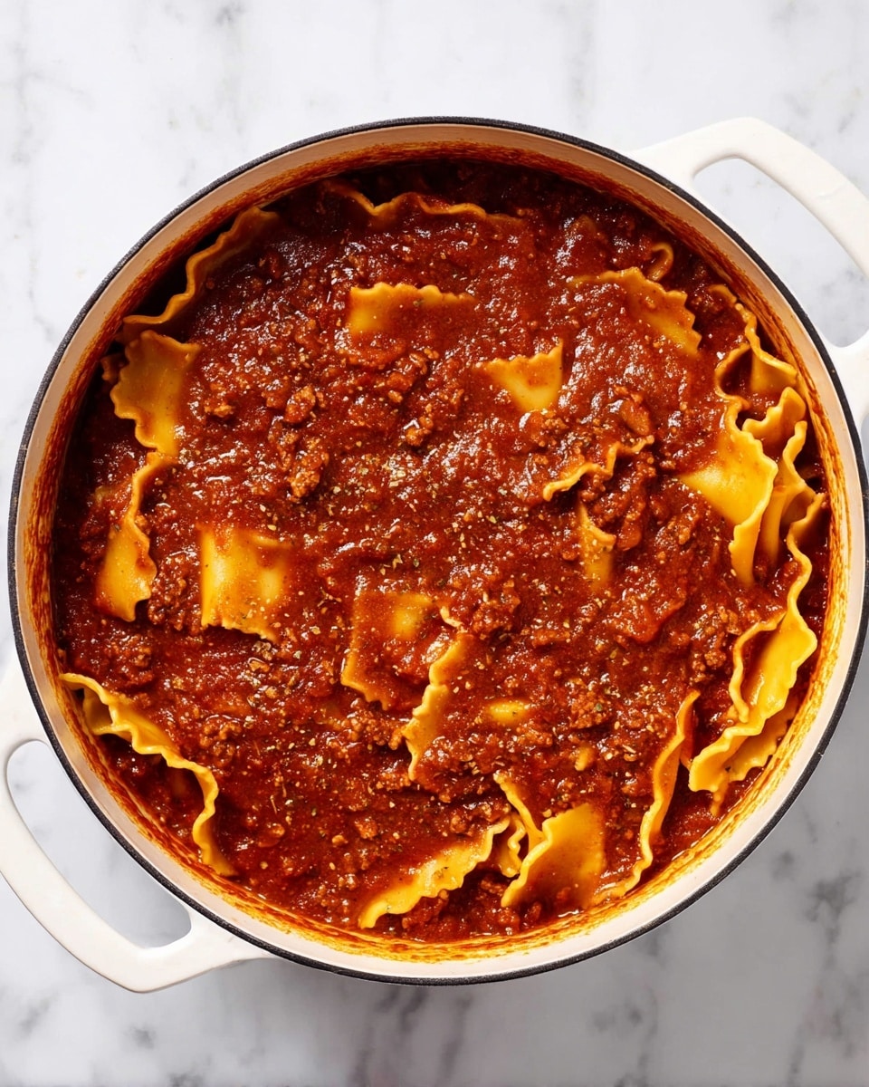 A white pot filled with thick, dark red tomato sauce that has small bits of ground meat and spices visible throughout. Inside the sauce, wide, wavy-edged, yellow pasta pieces are partially submerged and curled in different directions. The sauce surface looks smooth with some texture from the meat and herbs. The pot is on a white marbled surface, with the warm colors of the sauce contrasting against the clean, bright background. Photo taken with an iphone --ar 4:5 --v 7