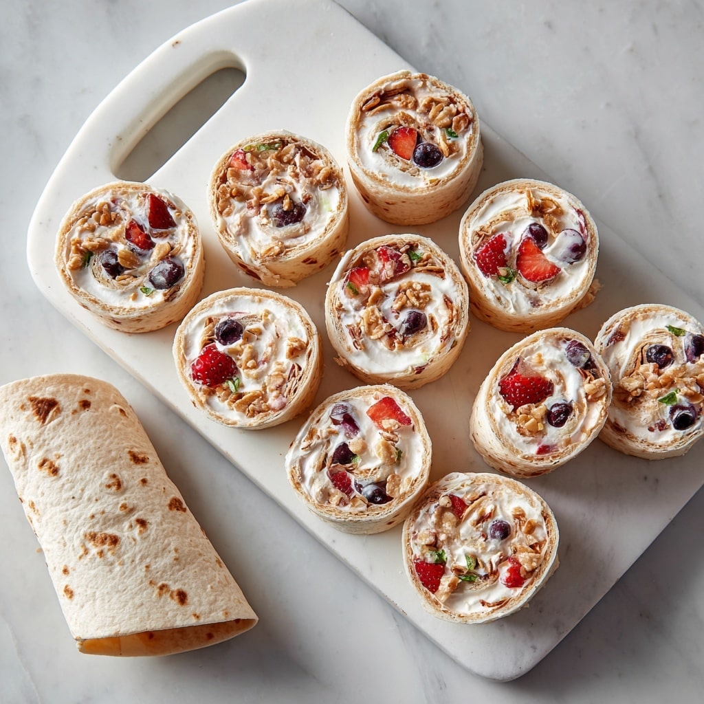 Nine round pinwheel rolls sit spread on a white cutting board with a handle at the top, placed on a white marbled surface. Each pinwheel shows visible layers: a soft light beige tortilla outer layer, a thick white cream cheese layer inside, chunks of red strawberries, green blueberries, and bits of brown granola sprinkled throughout. Below the pinwheels, a partially rolled-up tortilla wrap lies with light brown spots visible on the surface. The image has soft, natural lighting that highlights the textures and colors of the wrap and fruit. photo taken with an iphone --ar 4:5 --v 7