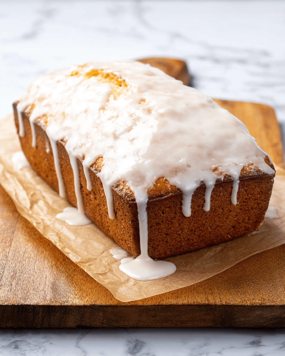 A rectangular golden-brown loaf cake with a slightly cracked top is covered in a thick, white glaze that drips down the sides and pools at the base. The cake sits on a piece of parchment paper, which is placed on a wooden board. The background is a white marbled surface. The glaze has a smooth, shiny texture and contrasts with the rougher texture of the cake’s crust photo taken with an iphone --ar 4:5 --v 7