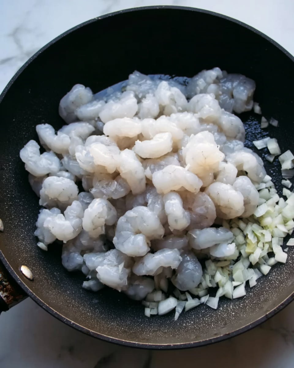 A close-up view of a black frying pan filled with many small pieces of raw shrimp piled in the center, their color pale translucent white with a slightly shiny, wet look. Underneath the shrimp, some small bits of white diced onion are scattered, contrasting with the smooth, soft texture of the shrimp. The frying pan rests on a surface, suggested now as a white marbled texture background. photo taken with an iphone --ar 4:5 --v 7