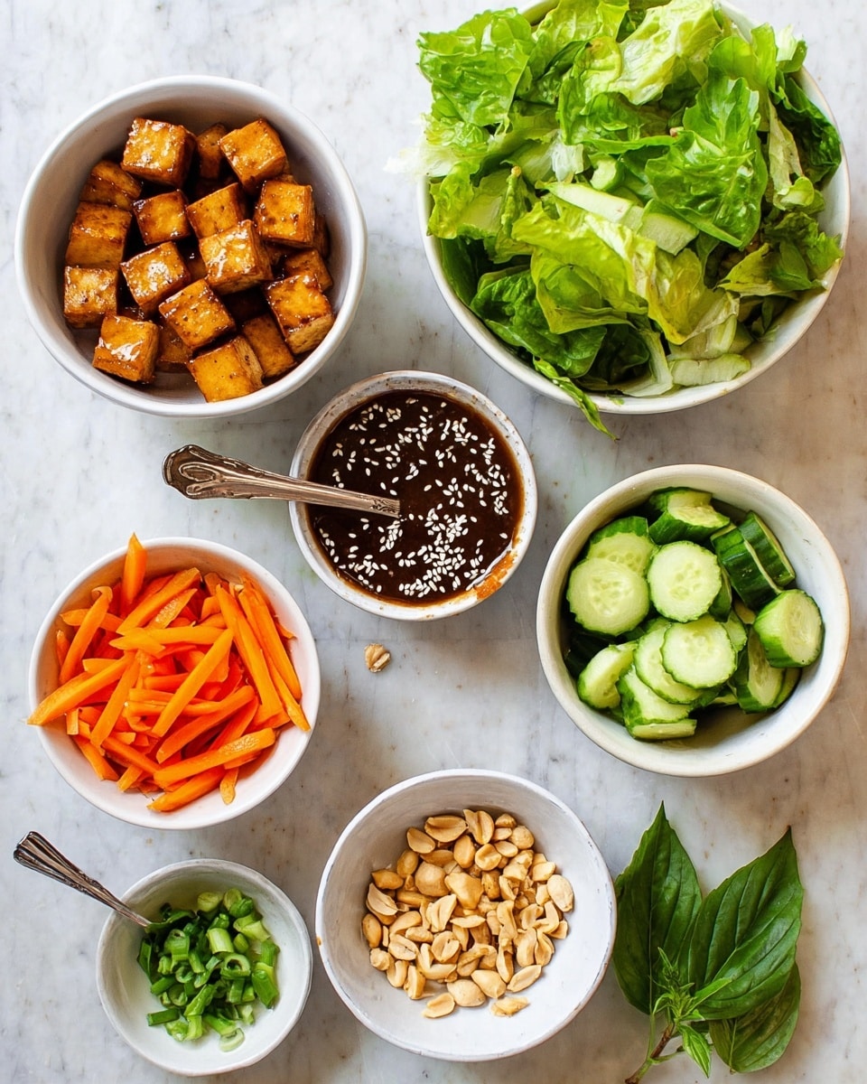 The image shows seven white bowls arranged on a white marbled surface. Starting from the top left, the first bowl contains golden brown tofu cubes, cooked with a slightly crispy texture. Next to it, there is a bowl filled with bright green lettuce leaves, fresh and torn. Below the tofu, there is a bowl of thin, bright orange carrot sticks. To the right of the carrots, there is a bowl with sliced cucumber, the slices showing dark green skin and pale green flesh. In the center, a bowl holds a dark brown sauce topped with white sesame seeds and a silver spoon. Below that, a small bowl contains chopped green onions, and to its right, another bowl has pale roasted peanuts. Two fresh green basil leaves lie on the surface between the bowls. Photo taken with an iphone --ar 4:5 --v 7