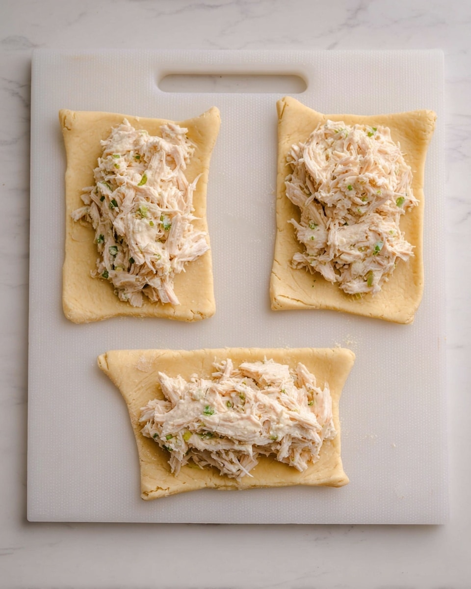 Three rectangular pieces of light golden dough are laid out on a white cutting board with a handle on the left side, placed on a white marbled surface. Each dough rectangle has a light creamy mixture of shredded chicken placed roughly in the middle. The dough texture looks soft and slightly wrinkled, while the shredded chicken mixture is fluffy and moist with small green flecks. The pieces are arranged so that two are horizontal at the top and bottom left, and one vertical on the right side. photo taken with an iphone --ar 4:5 --v 7