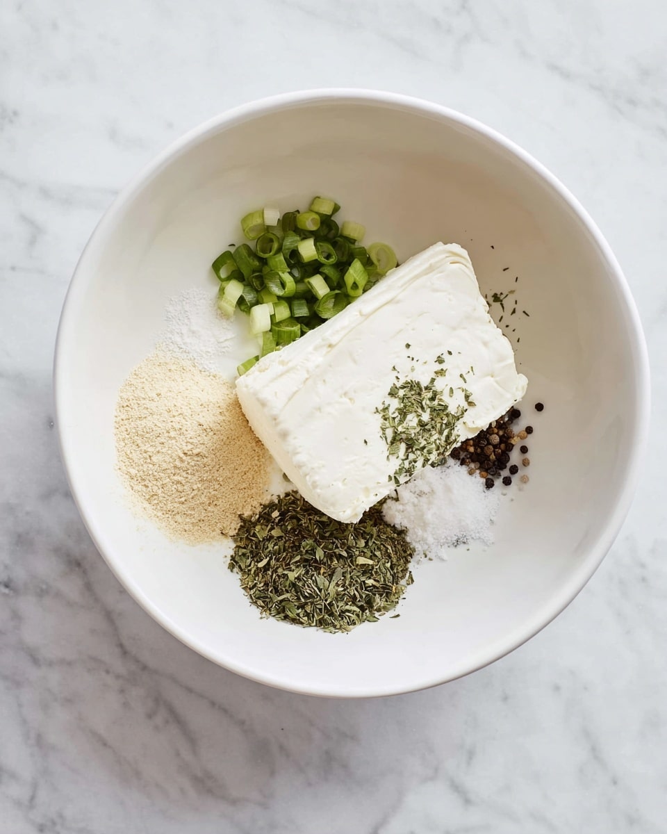 A white bowl on a white marbled surface holds a block of cream cheese positioned slightly off-center. Around the cream cheese, there are several seasonings: chopped green onions in the top left corner, a light beige powder at the bottom left, a mix of dark green dried herbs to the right, and a small pile of cracked black pepper near the center. The scene is bright and clean with a simple arrangement. Photo taken with an iphone --ar 4:5 --v 7