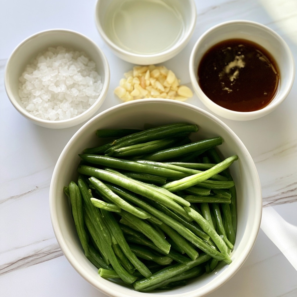 The image shows a close-up of a white bowl full of fresh green beans, placed on a white marbled surface. Above it, there are four small white bowls arranged in a loose semicircle, each containing a different ingredient: the top bowl has clear oil with a smooth surface, the right bowl holds a dark brown chicken broth concentrate with a shiny texture, the middle bowl contains small, chopped pieces of pale yellow garlic, and the left bowl is filled with coarse white salt crystals in a slightly translucent container. Each ingredient is clearly visible with natural light brightening the scene. Photo taken with an iphone --ar 4:5 --v 7