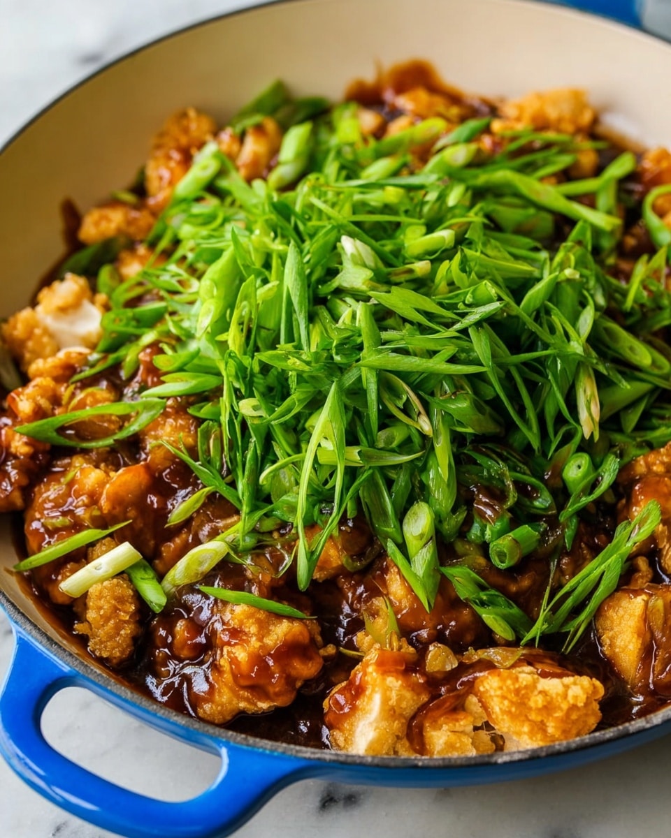 A close-up image shows a white skillet with a blue handle on a white marbled surface. Inside the skillet, there are two main layers: the bottom layer has small pieces of light golden fried chicken coated in a shiny, rich brown sauce. On top, there is a thick pile of fresh, bright green chopped green onions, cut into short stalks, providing a vibrant contrast. The sauce glistens, covering much of the chicken, and the green onions add a fresh, crisp look. Photo taken with an iphone --ar 4:5 --v 7