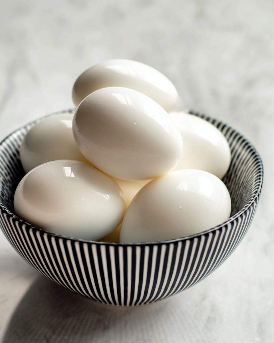 A white bowl with thin black vertical stripes holds a cluster of smooth, shiny boiled eggs stacked closely together, showing their clean white shell texture. The background surface is a white marbled texture, and the image is focused closely on the eggs with soft natural light highlighting their round shape and slight reflections on the shells. photo taken with an iphone --ar 4:5 --v 7
