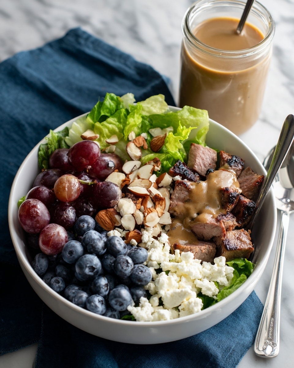 A white bowl is filled with a layered dish starting at the bottom with fresh green lettuce leaves. On the right side, there is a layer of white crumbled cheese with some brown sauce drizzled over it. Below the cheese and lettuce, there is a layer of cooked, sliced chicken pieces that are light brown and covered with a creamy brown dressing. Above the chicken, near the top right, is a cluster of dark blue blueberries. On the left side, on top of the lettuce, are small pieces of chopped nuts, likely almonds, mixed with more dressing. A silver spoon rests inside the bowl on the right side, and the background shows a white marbled texture. photo taken with an iphone --ar 4:5 --v 7