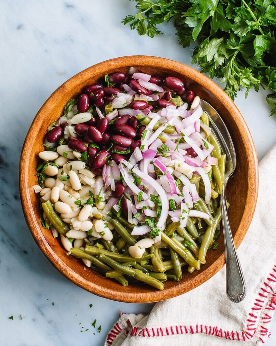The image shows a close-up of a colorful salad in a white bowl, placed on a white marbled surface. The salad has several visible layers and ingredients: green beans cut into short pieces giving a green texture, dark red kidney beans scattered throughout, small white beans adding lightness, and thin slices of red onion that create a bright purple contrast. The salad is topped with small chopped green herbs that add freshness. The colors and textures blend to make a fresh and vibrant looking dish photo taken with an iphone --ar 4:5 --v 7
