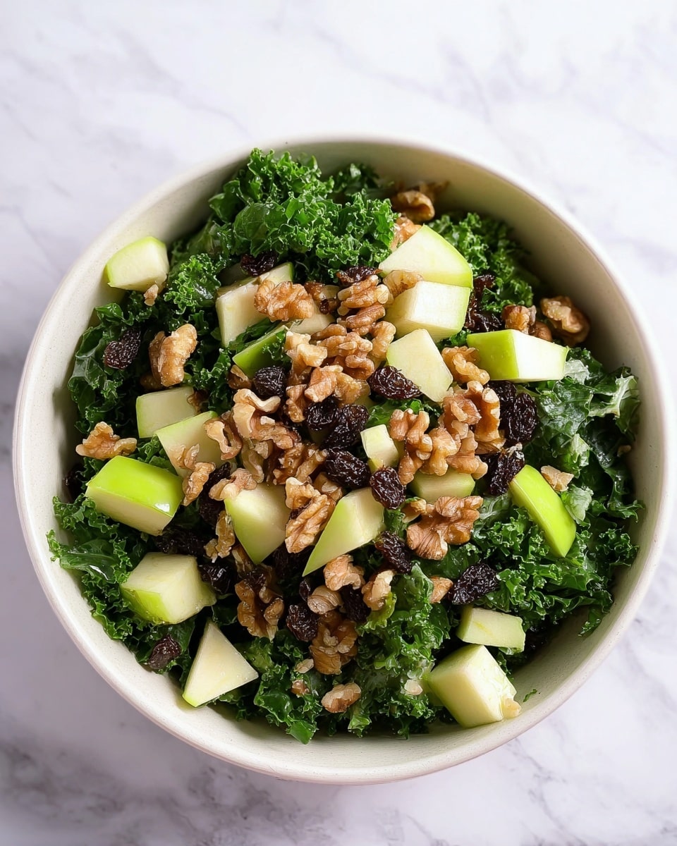 A white bowl holds a fresh kale salad with deep green, curly kale leaves as the base layer. Scattered on top are light green apple cubes with pale creamy flesh that add a crisp texture. Small dark brown raisins are mixed in evenly, adding a chewy contrast. The top layer features clusters of light to medium brown walnuts, enhancing the salad with a rough texture. The bowl is set on a white marbled surface, highlighting the vibrant colors of the salad. photo taken with an iphone --ar 4:5 --v 7