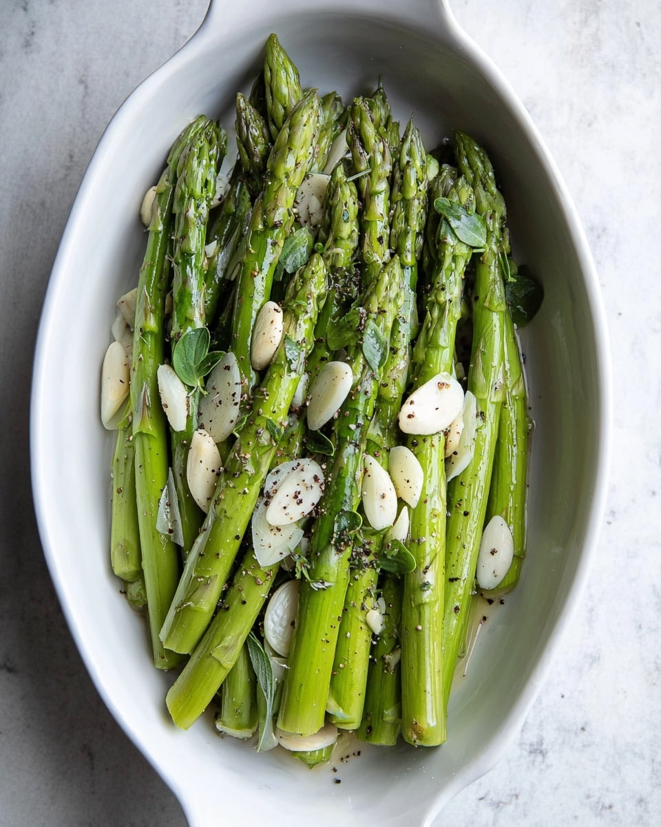 A white oval dish holds a single layer of fresh green asparagus spears, arranged side by side with tips pointing upward and slightly overlapping. Thin, light cream slices of garlic are scattered evenly across the asparagus. Small green herb leaves are sprinkled throughout, with black pepper flakes dotting the whole surface. The dish sits on a white marbled texture background. photo taken with an iphone --ar 4:5 --v 7
