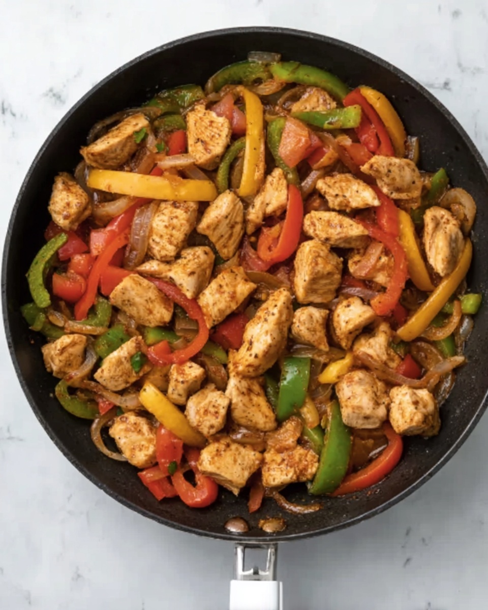 A black pan filled with cooked pieces of light brown chicken placed on top of a colorful mix of sliced vegetables including yellow, green, and red bell peppers, as well as chopped red tomatoes and light brown onion slices. The vegetables appear soft and mixed with light sauce, showing a glossy texture under bright light. The pan handle is white, resting on a white marbled surface visible in the background. The photo taken with an iphone --ar 4:5 --v 7