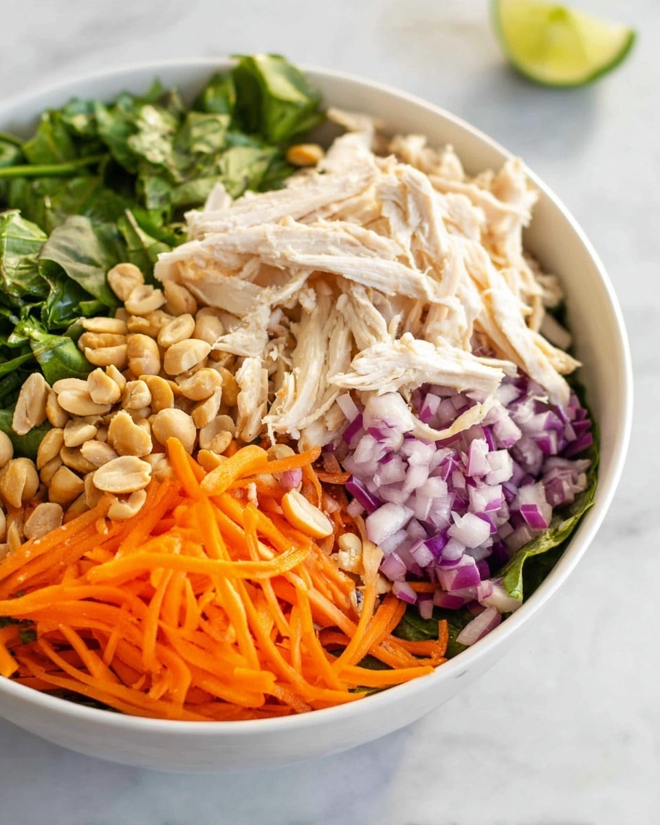 A white bowl filled with six visible layers: starting with a base of green leafy herbs to the left, followed by shredded orange carrots in the bottom right corner, thinly sliced purple onions slightly above the carrots, chopped light brown peanuts in the center, and a pile of shredded pale beige chicken on top at the back of the bowl, against a white marbled surface background. A small wedge of lime can be seen blurred in the background. photo taken with an iphone --ar 4:5 --v 7