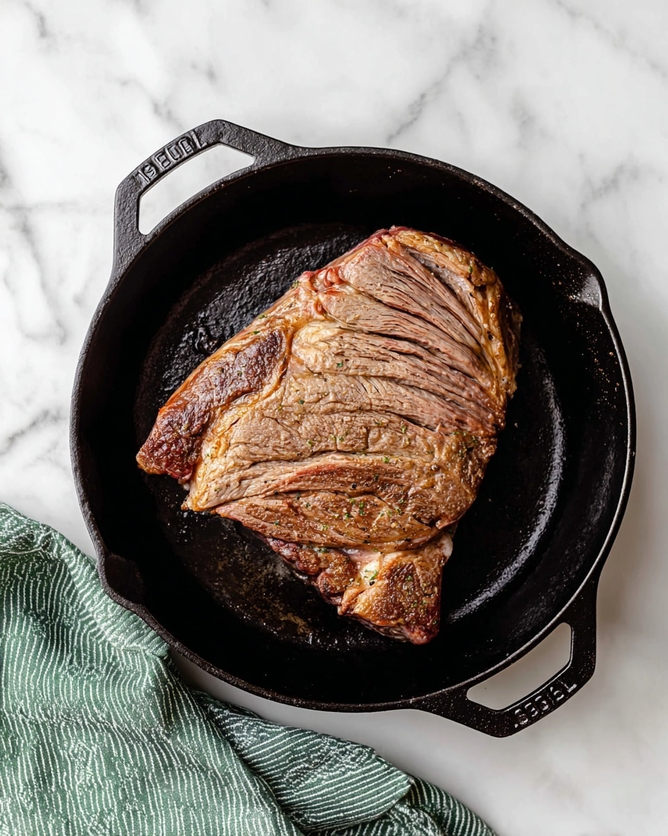 A large piece of cooked meat with a brown, slightly crispy outside is placed in the center of a black cast iron pan. The meat has visible muscle fibers and some light pink areas showing inside. The pan is round with two small handles on the sides, sitting on a surface with a white marble texture. On the bottom left corner, part of a green cloth with white stripes is visible. photo taken with an iphone --ar 4:5 --v 7