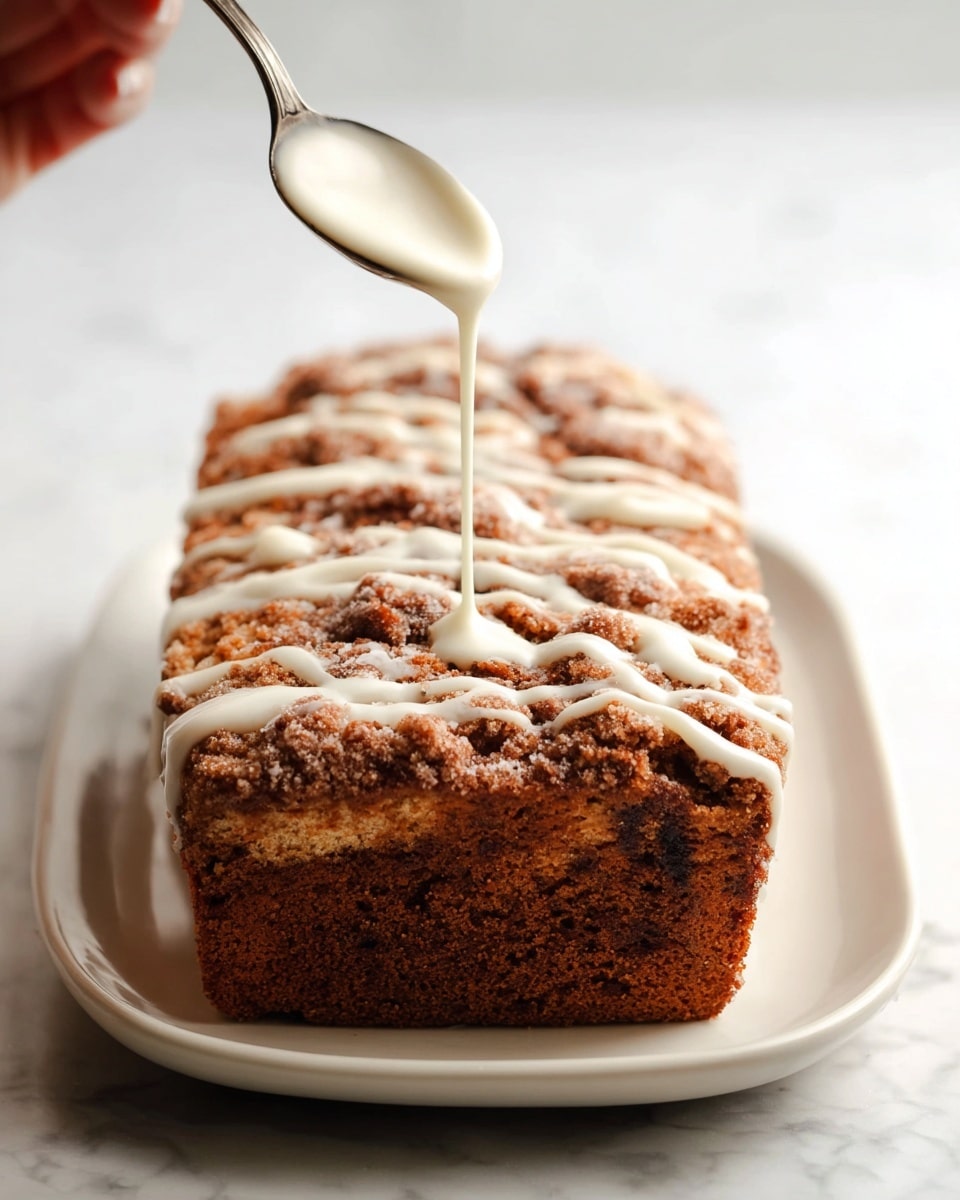 A rectangular loaf with a rough, crumbly brown topping sits centered on a white plate. The top layer has a mixture of light and dark brown crumb textures, uneven and slightly chunky. A woman's hand holds a spoon pouring smooth white icing in thin lines across the top of the loaf. The background surface is a white marbled texture, giving a clean and bright setting. Photo taken with an iphone --ar 4:5 --v 7