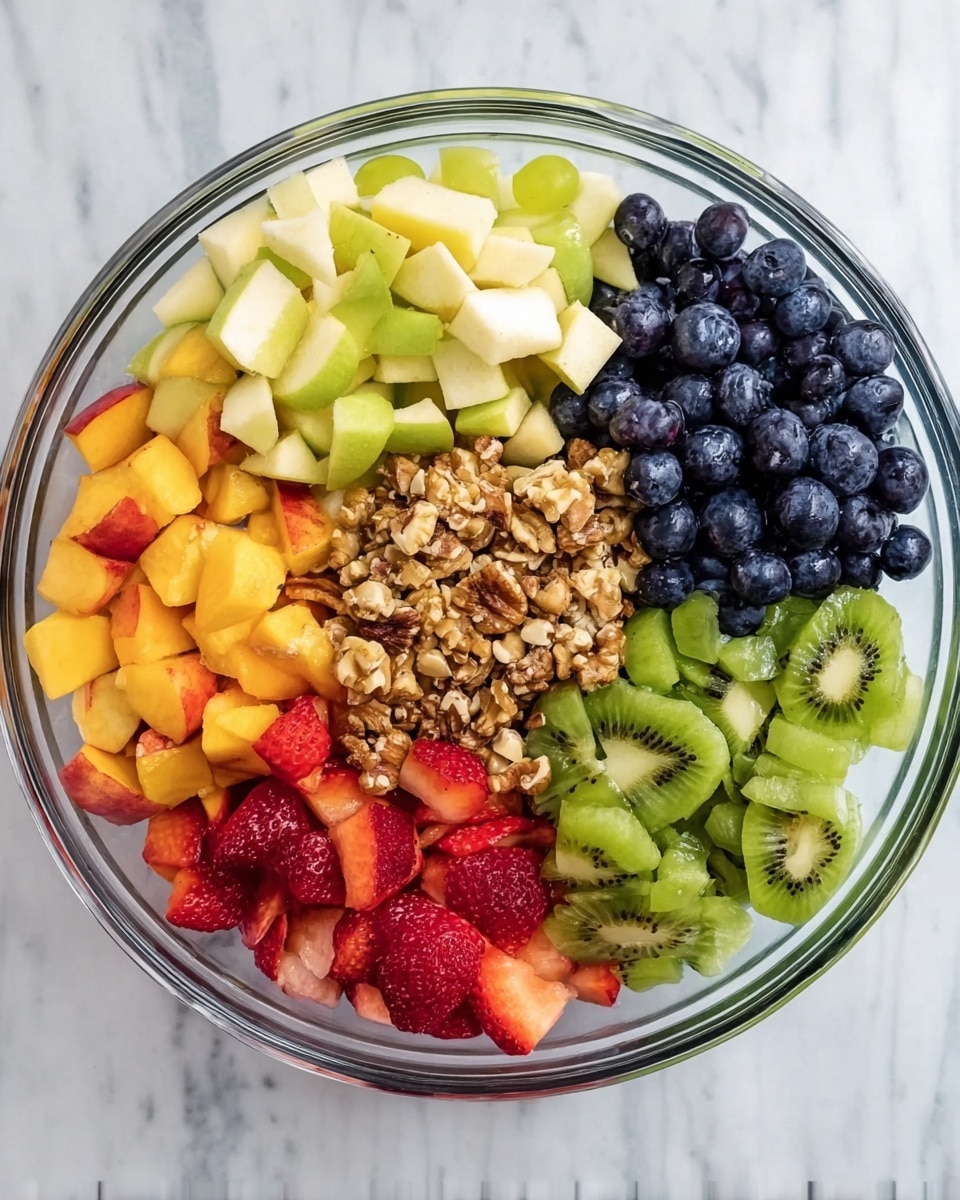 A clear glass bowl holds seven sections of fresh fruit and chopped nuts arranged neatly. Starting from the top and moving clockwise, there are light yellow apple pieces with smooth texture, dark blue blueberries that look round and plump, bright green grapes that are shiny and smooth, a pile of light brown chopped nuts with a rough texture, orange peaches cut into chunks, red strawberries sliced into thin pieces showing their juicy interior, and finally, green kiwi slices that show a speckled black seed pattern and juicy flesh. All of this is set on a white marbled surface. Photo taken with an iphone --ar 4:5 --v 7