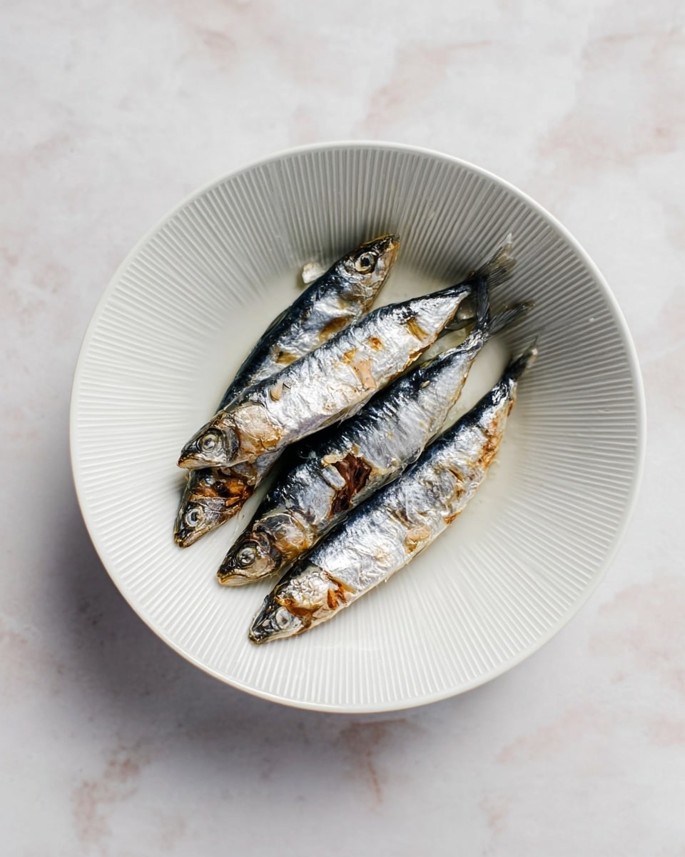 A white bowl with fine vertical lines on the inner surface holds five small, shiny sardines arranged loosely in the center. The sardines have a silver-blue color with darker stripes and patches, and their skin looks moist and slightly oily, reflecting light softly. The bowl sits on a white marbled surface, creating a clean and simple look. photo taken with an iphone --ar 4:5 --v 7