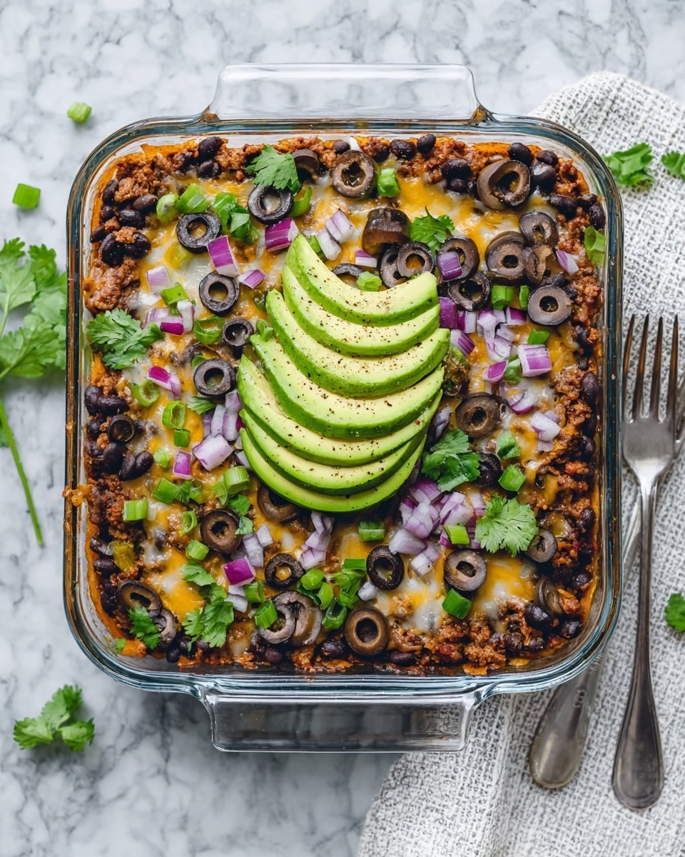 A square glass dish shows a layered baked dish with a white marbled surface underneath. The bottom layer looks like cooked ground meat mixed with black beans spread evenly. On top, there is melted cheese, dark brown sliced olives, chopped green onions, and small pieces of purple onion scattered all around. Fresh green cilantro leaves add color across the surface. In the center, there is a fan of thinly sliced avocado with a light sprinkle of black pepper. A white cloth with a silver fork rests to the right side of the dish. Photo taken with an iphone --ar 4:5 --v 7